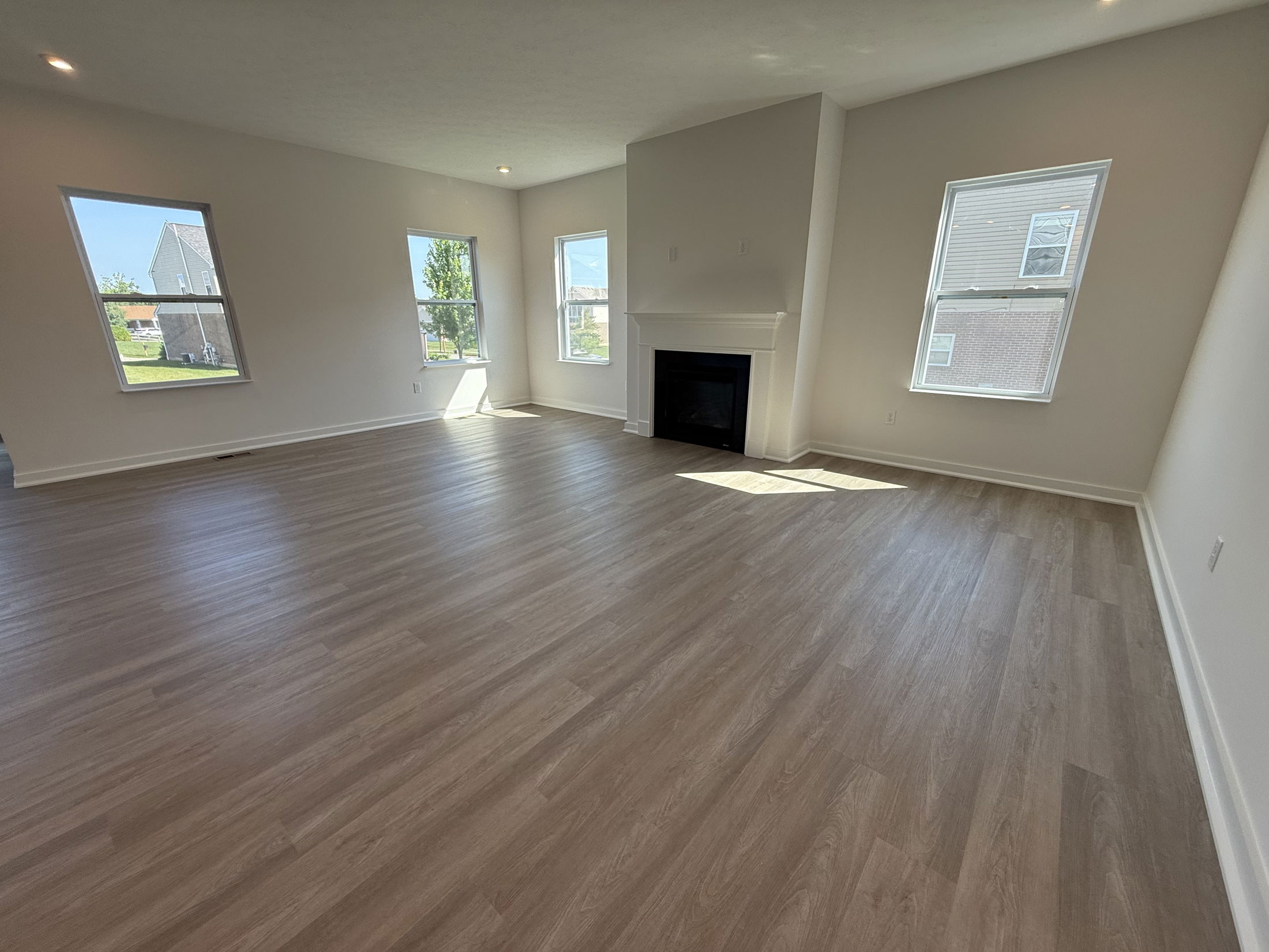 Spacious modern living room with light wood flooring, large windows, and a central fireplace, showcasing natural light and open space.