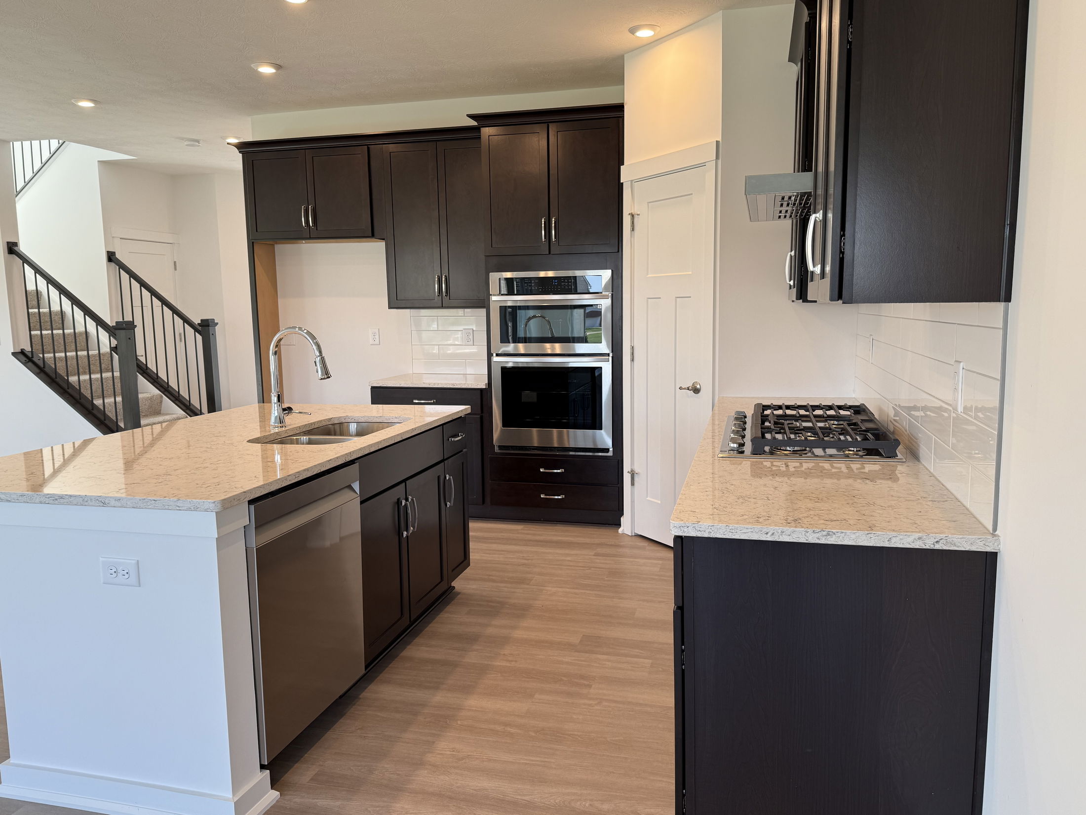 Modern kitchen with dark wood cabinets, white countertops, stainless steel appliances, and a central island sink.