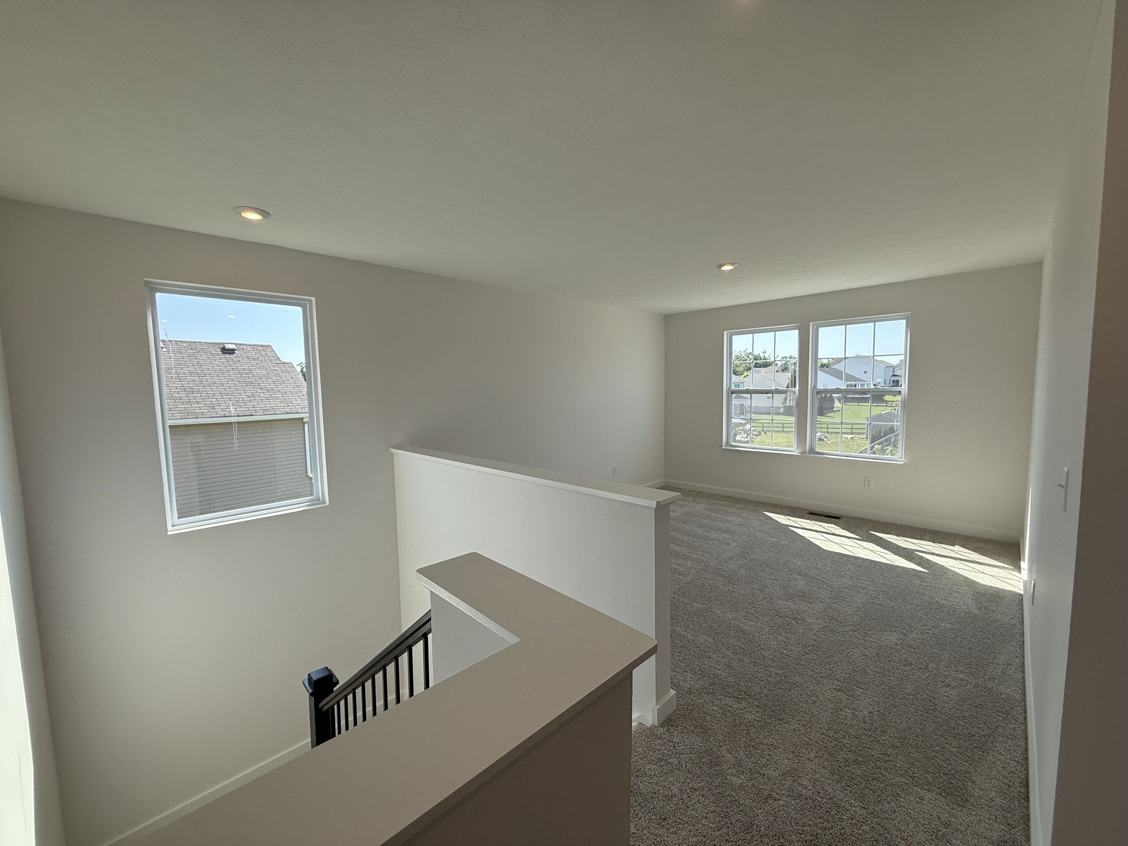 Bright, open loft space with large windows and carpeted flooring in a modern home.