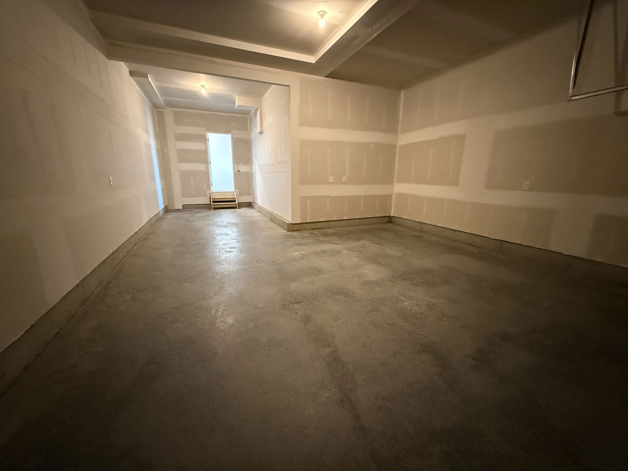 Empty residential garage with unfinished walls and concrete floor, under recessed lighting.