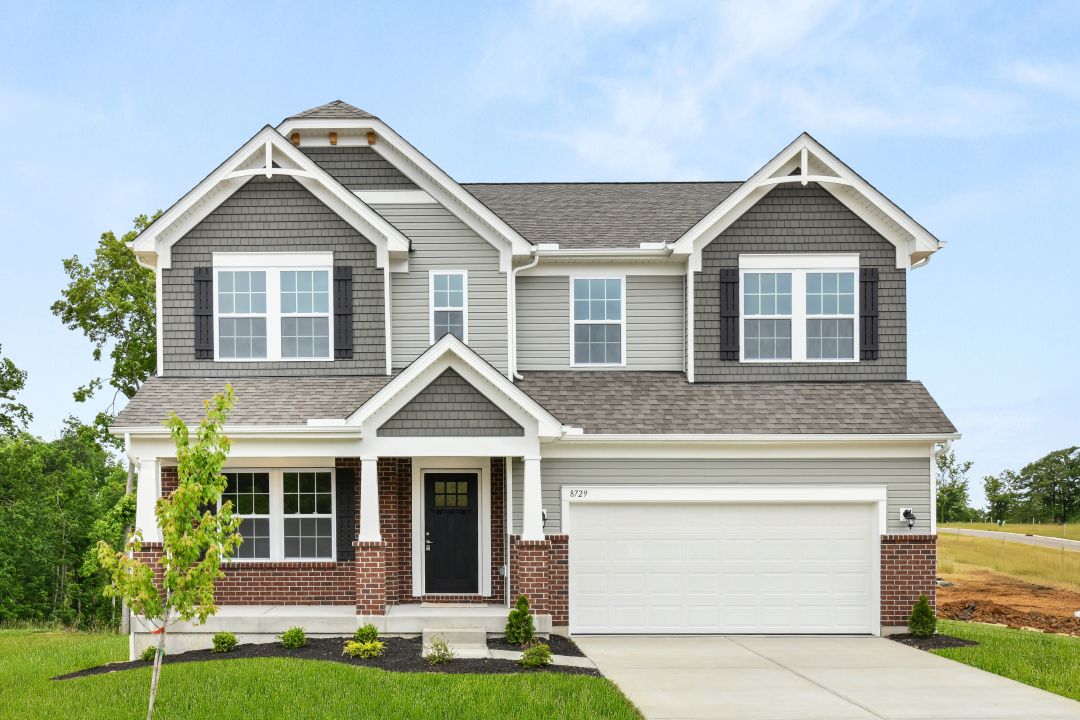 Front view of a modern two-story house with gray siding, brick accents, and a two-car garage, set against a clear blue sky.