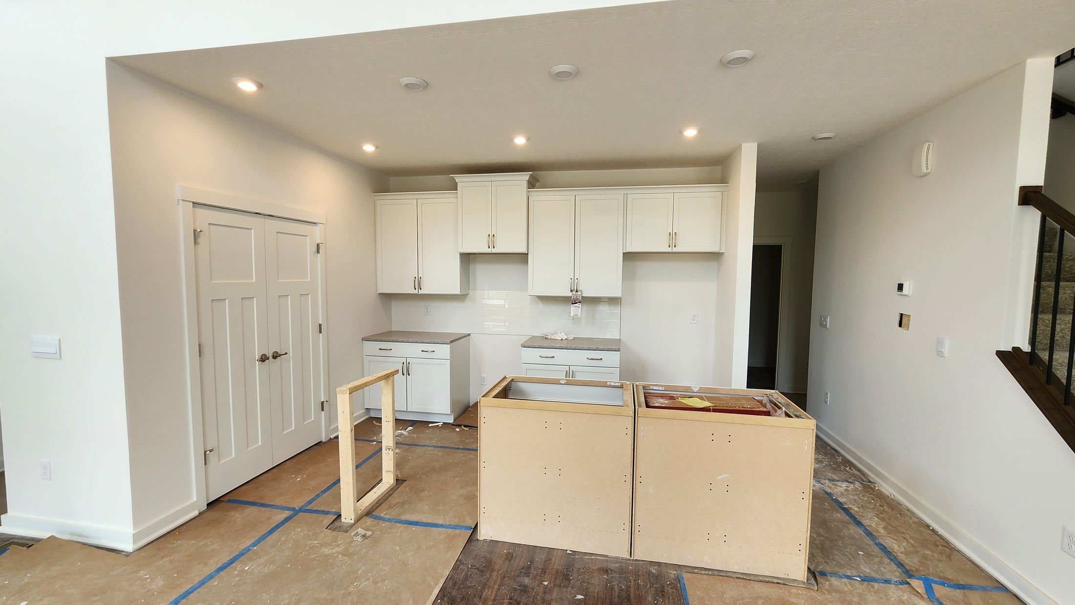 Modern kitchen under construction with white cabinets, recessed lighting, and a partially installed island.
