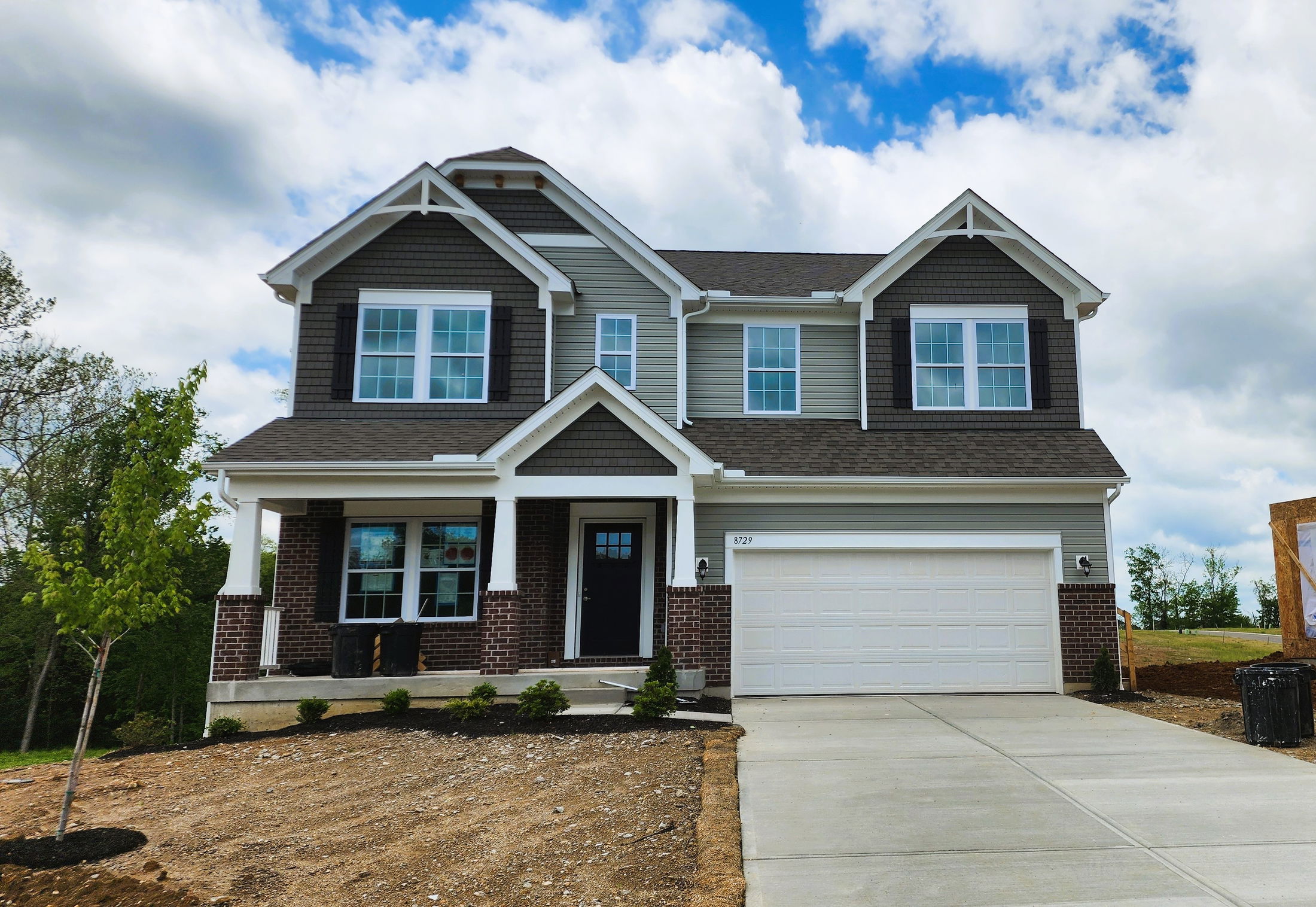 Two-story suburban house with a two-car garage, brick and siding exterior, and a neat front lawn under a partly cloudy sky.