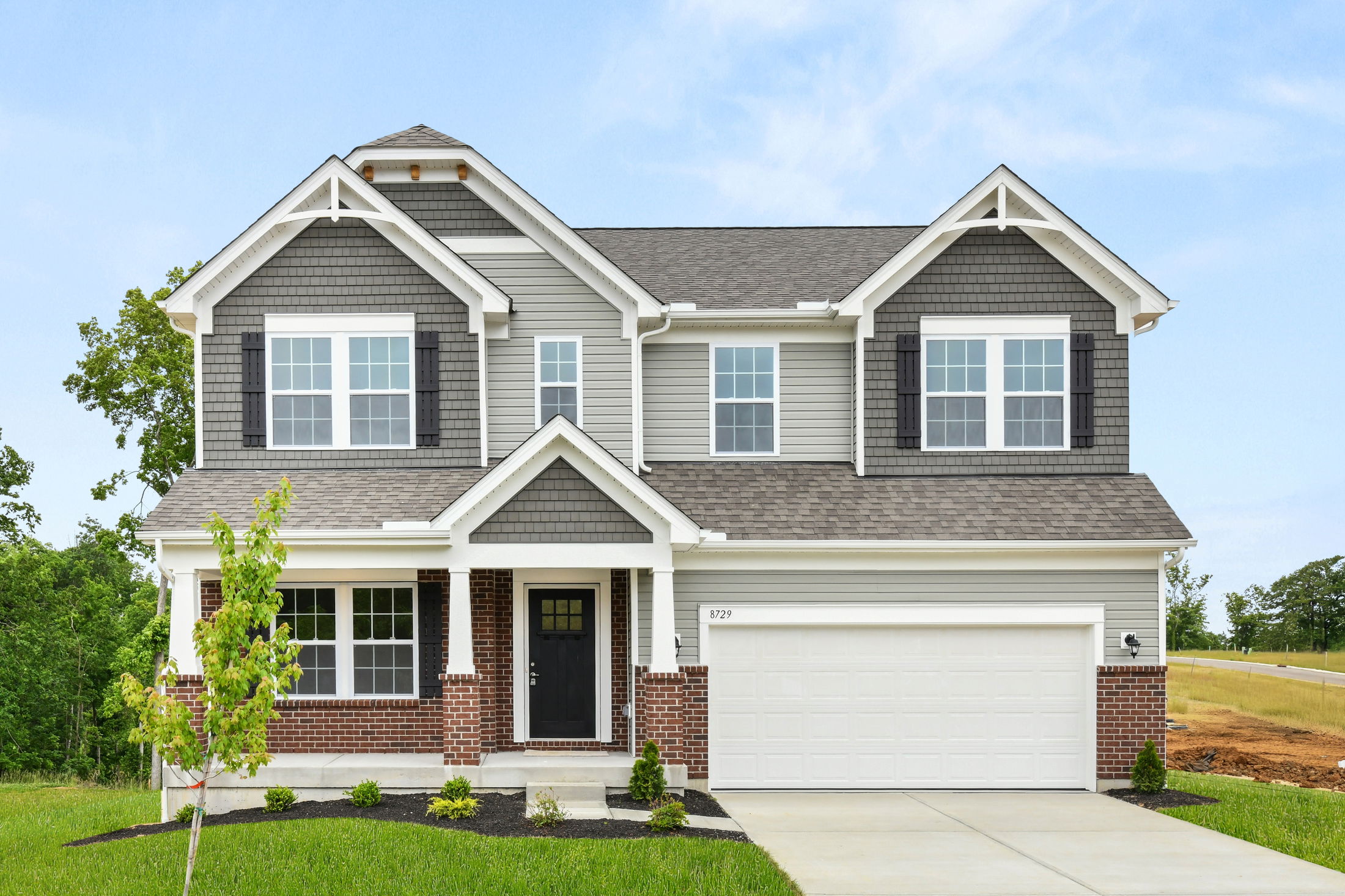 A modern two-story house with gray siding, dark shutters, a brick façade, and a spacious white garage.