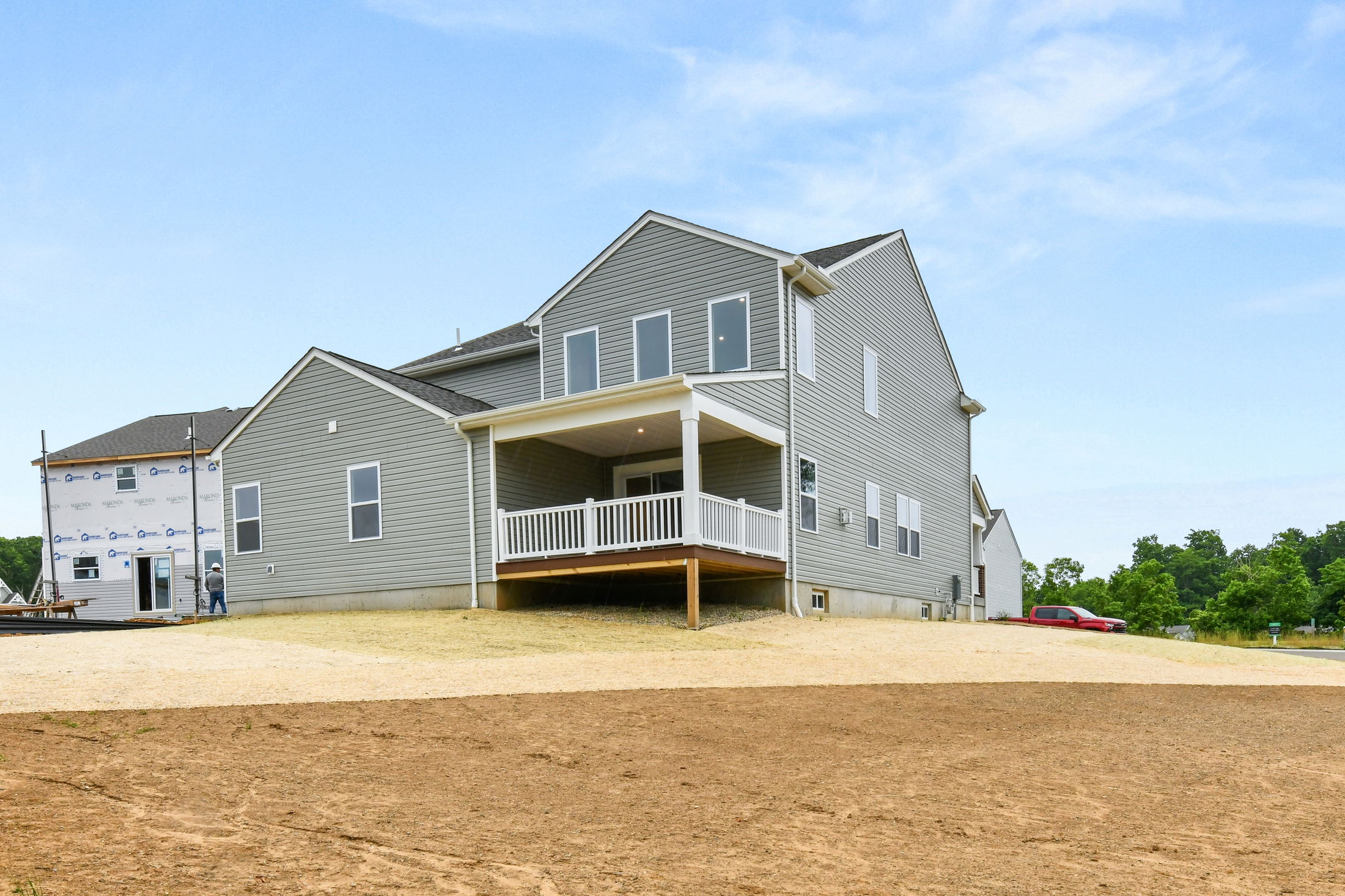 Newly constructed gray two-story house with a covered porch and spacious backyard under a clear blue sky.