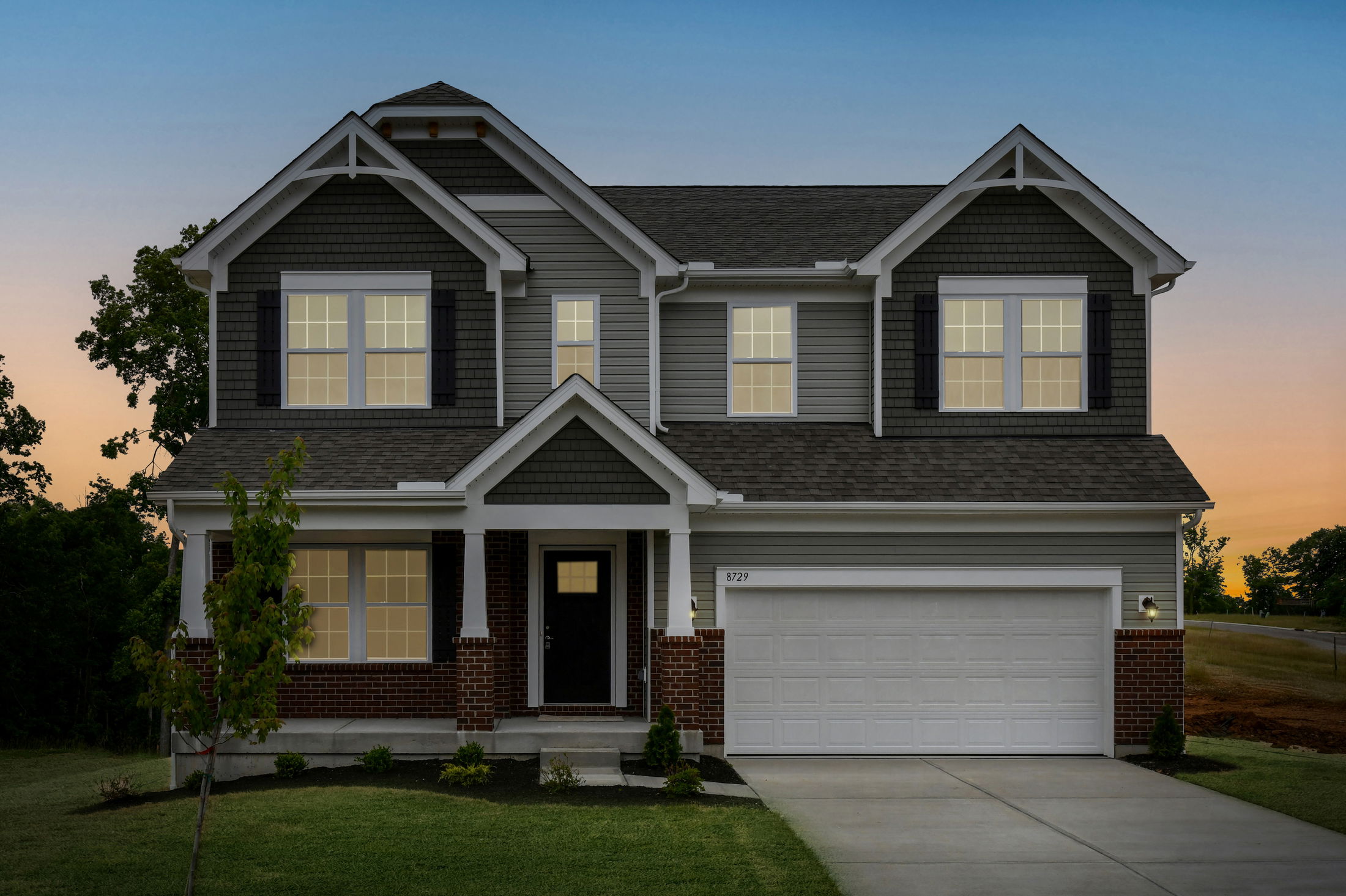 Modern two-story suburban home with gray siding, white trim, and a brick facade at sunset.