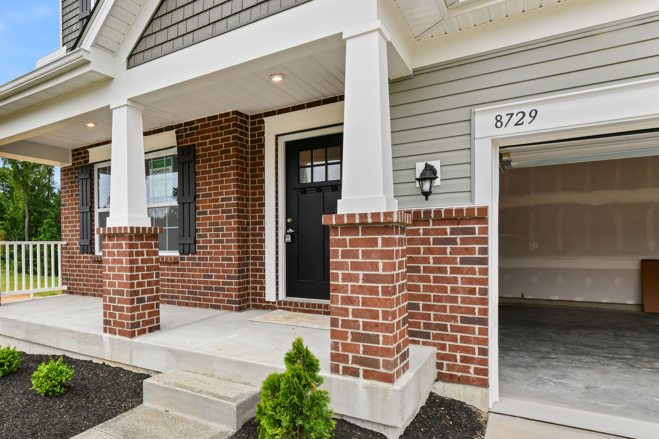 Front entrance of a modern brick house with a black door and partially open garage.
