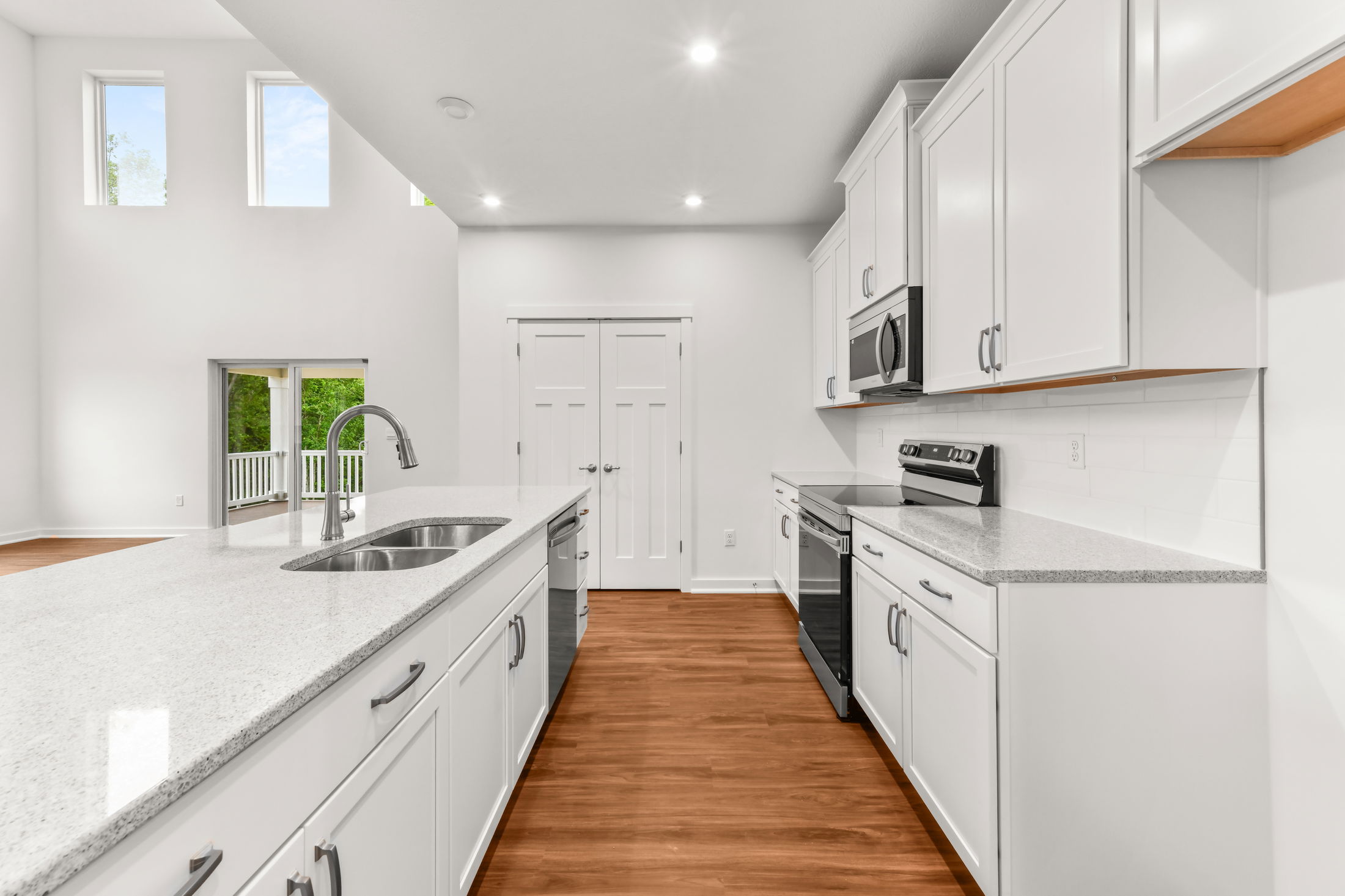 Modern kitchen with white cabinets, stainless steel appliances, and a spacious island with a built-in sink, featuring hardwood floors and bright natural lighting.