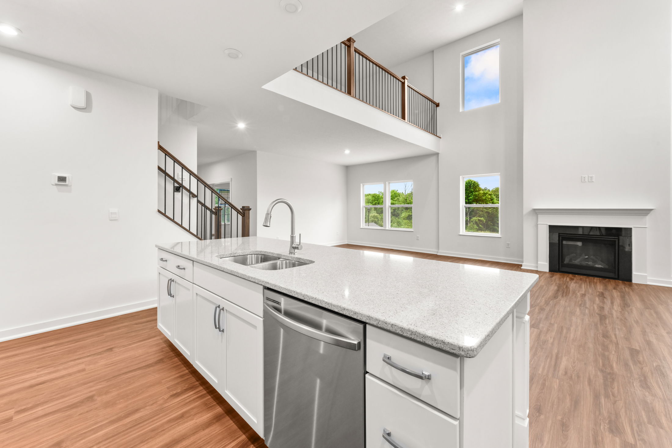 Modern open-concept kitchen and living area with white cabinetry, granite countertops, wood flooring, and large windows.