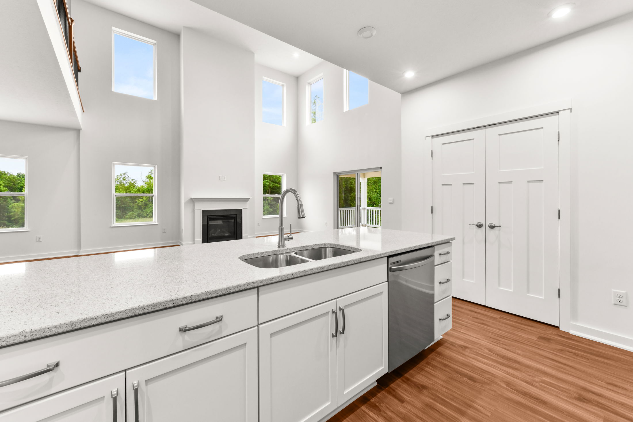 Modern open-concept kitchen with white cabinetry, sleek countertops, and a view of a spacious living area featuring large windows and a fireplace.