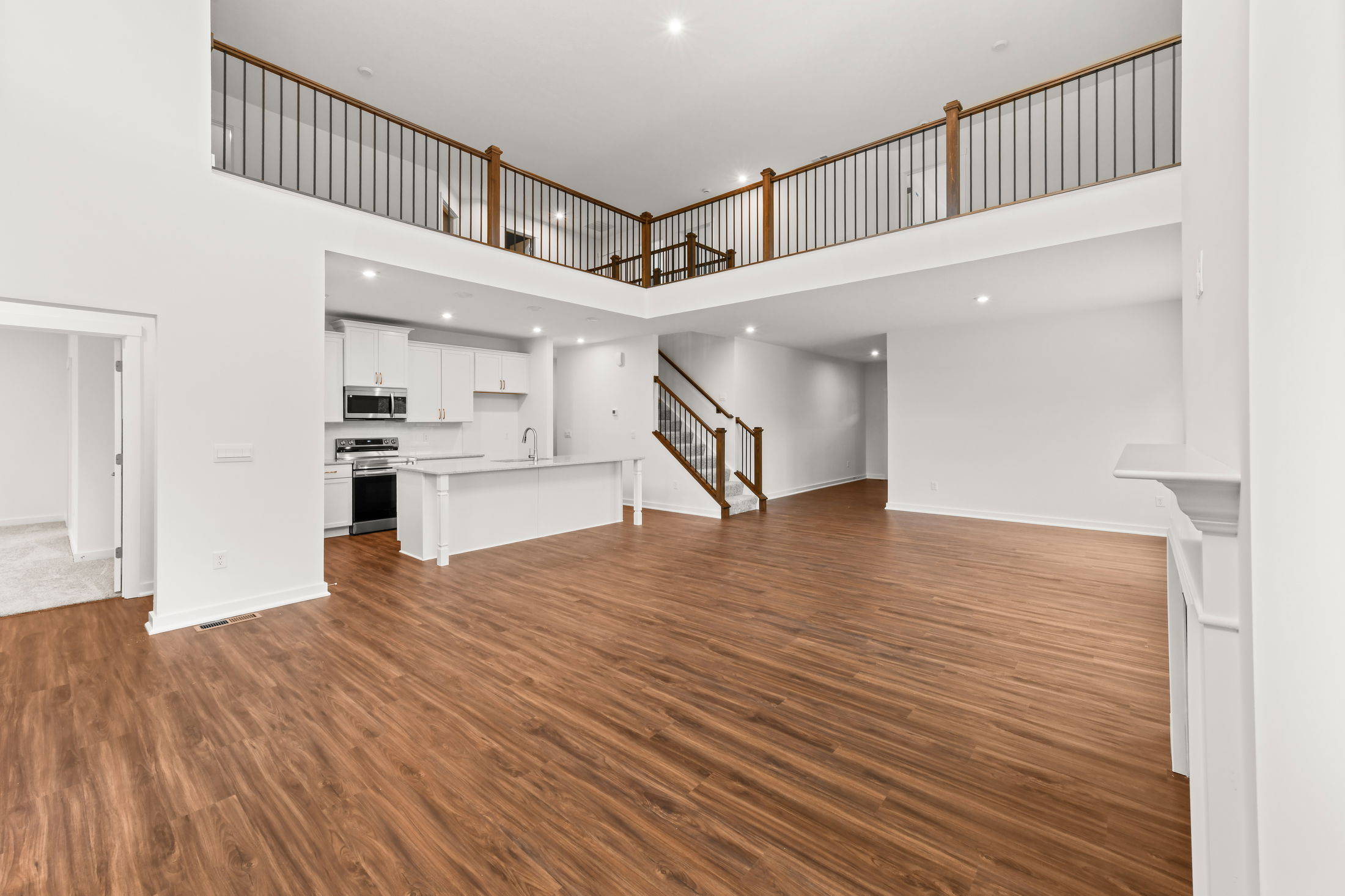 Modern open-concept living space with hardwood floors, kitchen island, and upstairs balcony view.