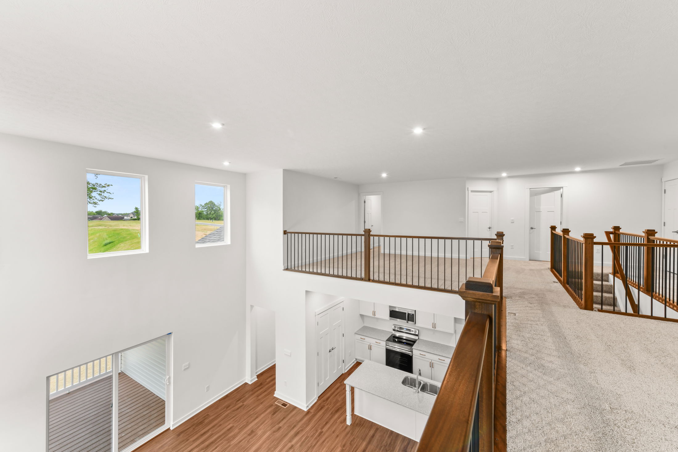 Modern open-concept home interior featuring an upper-level balcony, spacious living area, and a sleek kitchen with stainless steel appliances.