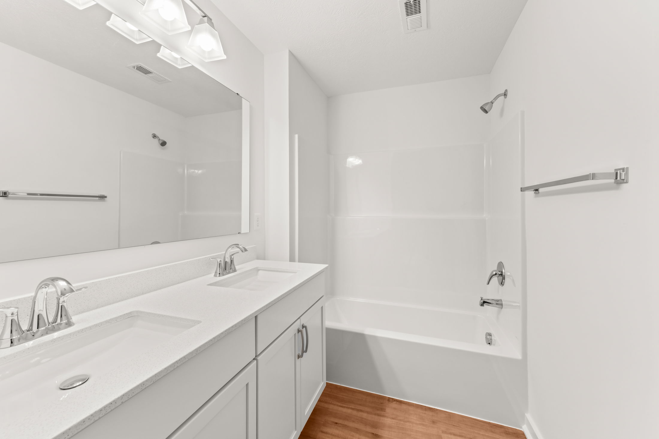 Modern white bathroom with double sinks, large mirror, and a shower-tub combo.