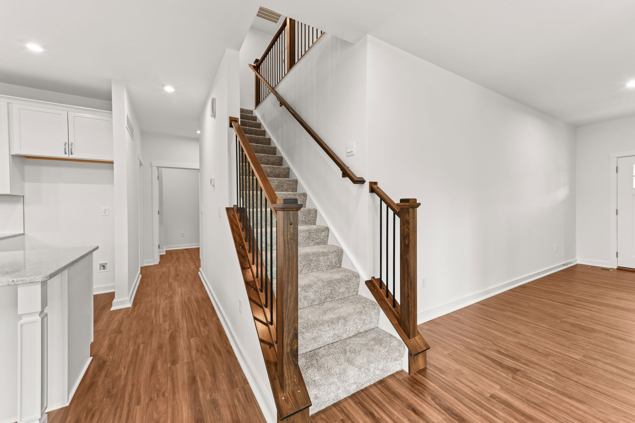 Modern interior view featuring a staircase with wooden handrails, carpeted steps, and hardwood flooring leading to an open hallway.