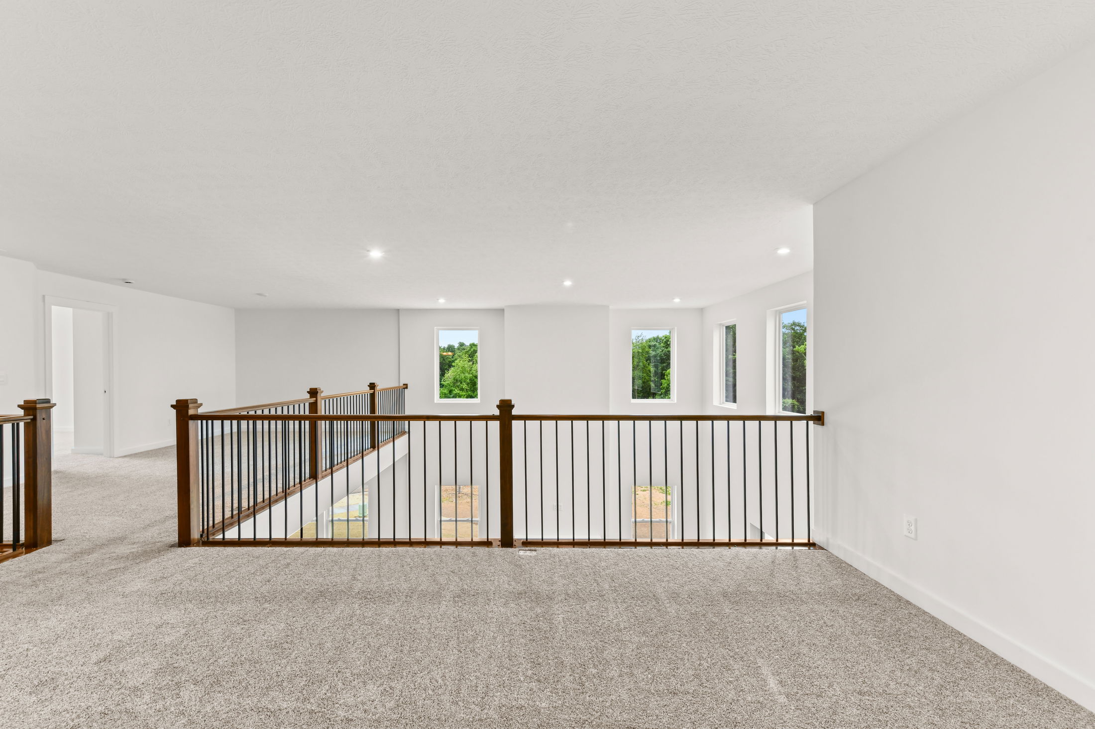 Spacious, carpeted second-floor landing with wooden railings and large windows offering natural light.