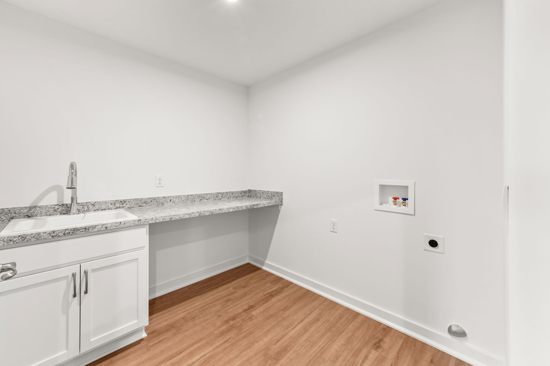 Modern laundry room with white cabinets, granite countertops, and wood flooring.