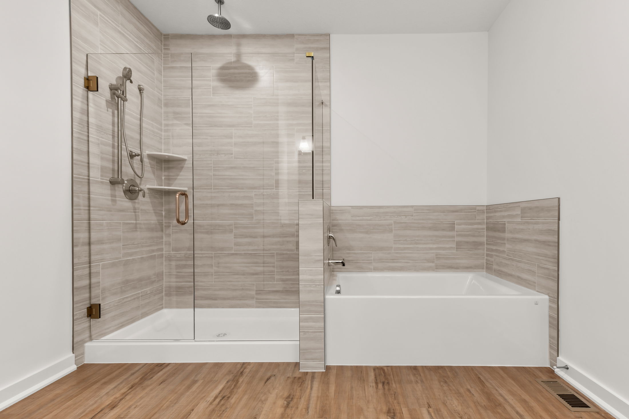 Modern bathroom with a glass-enclosed shower and adjacent bathtub, featuring beige tile and wood-style flooring.