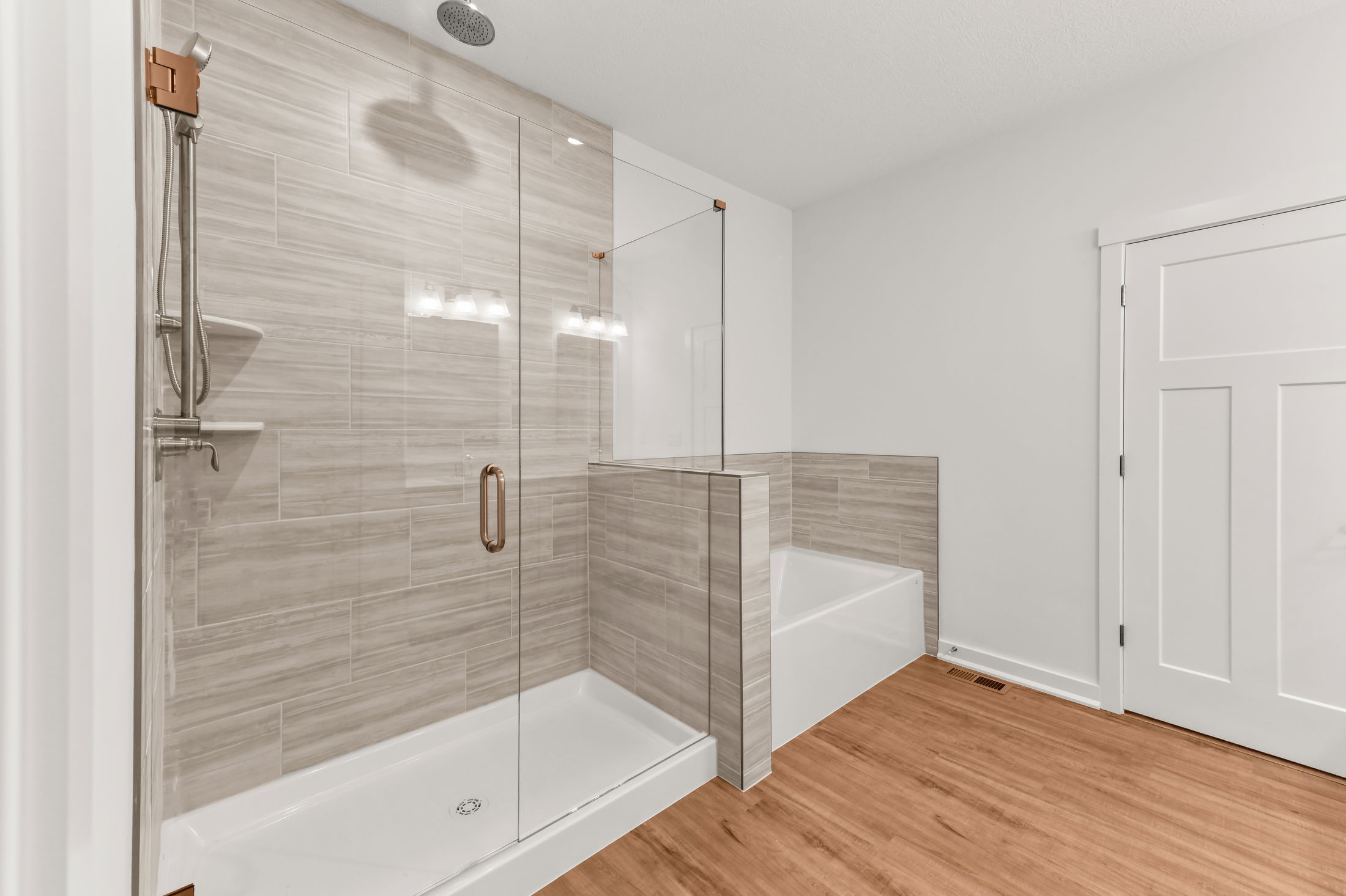 Modern bathroom with glass-enclosed shower, bathtub, wood flooring, and beige tiled walls.