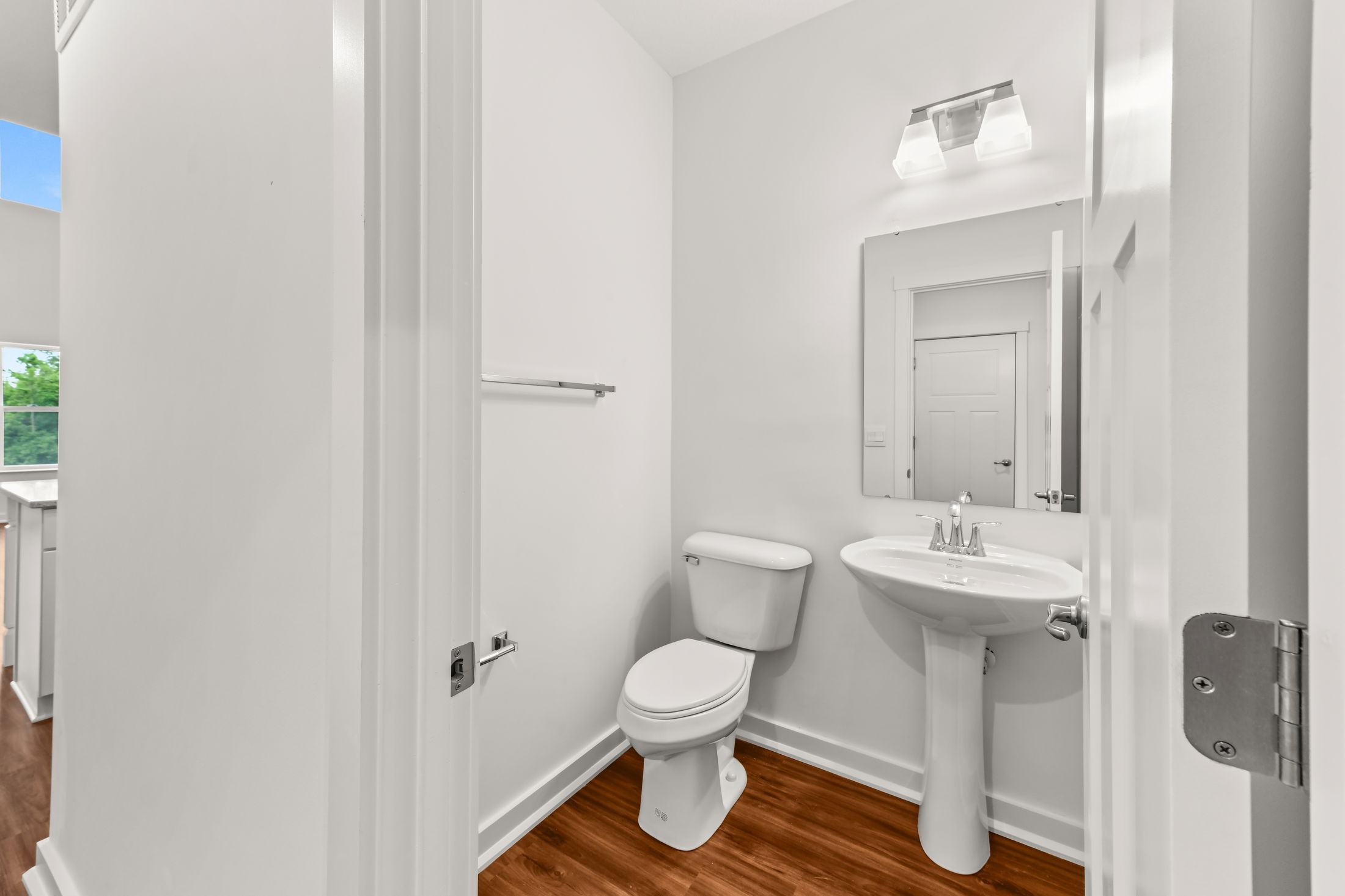 Modern white bathroom with a pedestal sink, toilet, and hardwood flooring.