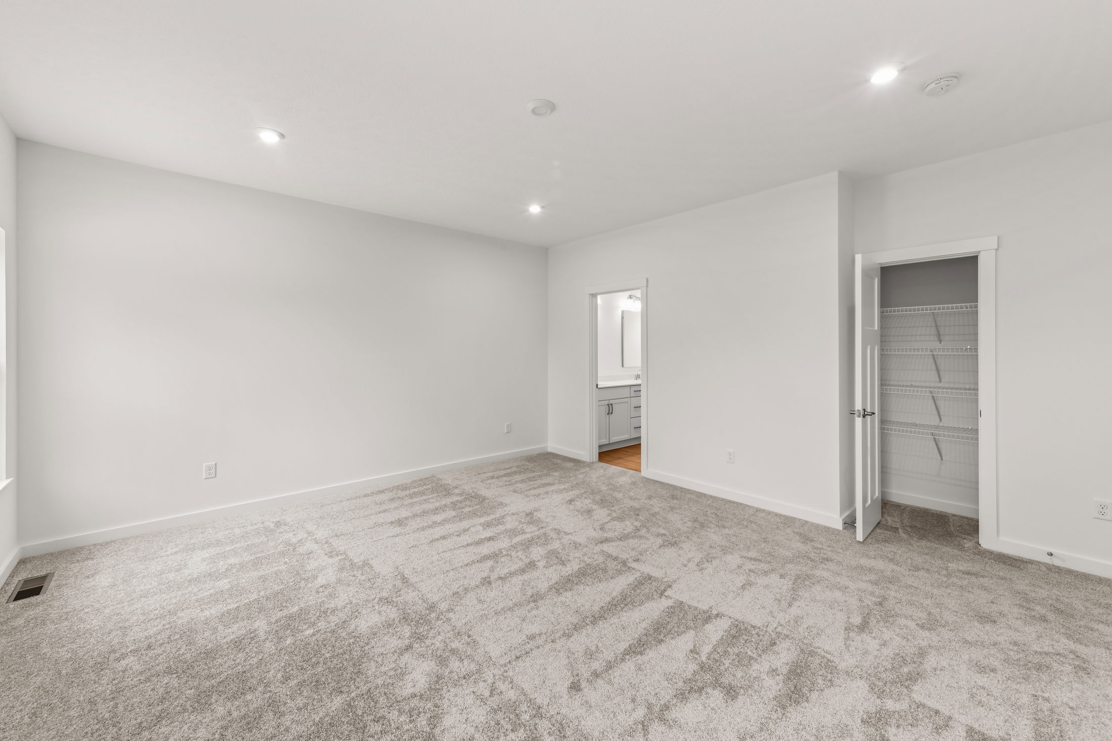 Spacious empty room with fresh gray carpet, a modern recessed lighting, and open closet leading to bathroom area.