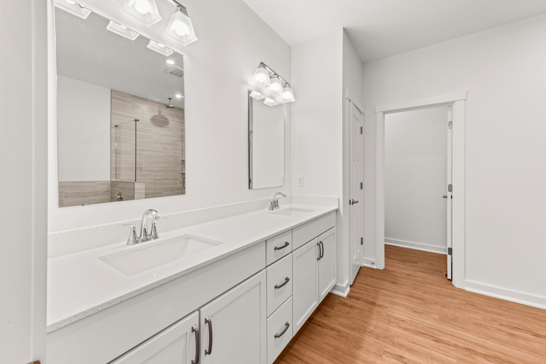 Modern bathroom with double vanity, white cabinets, and hardwood flooring.