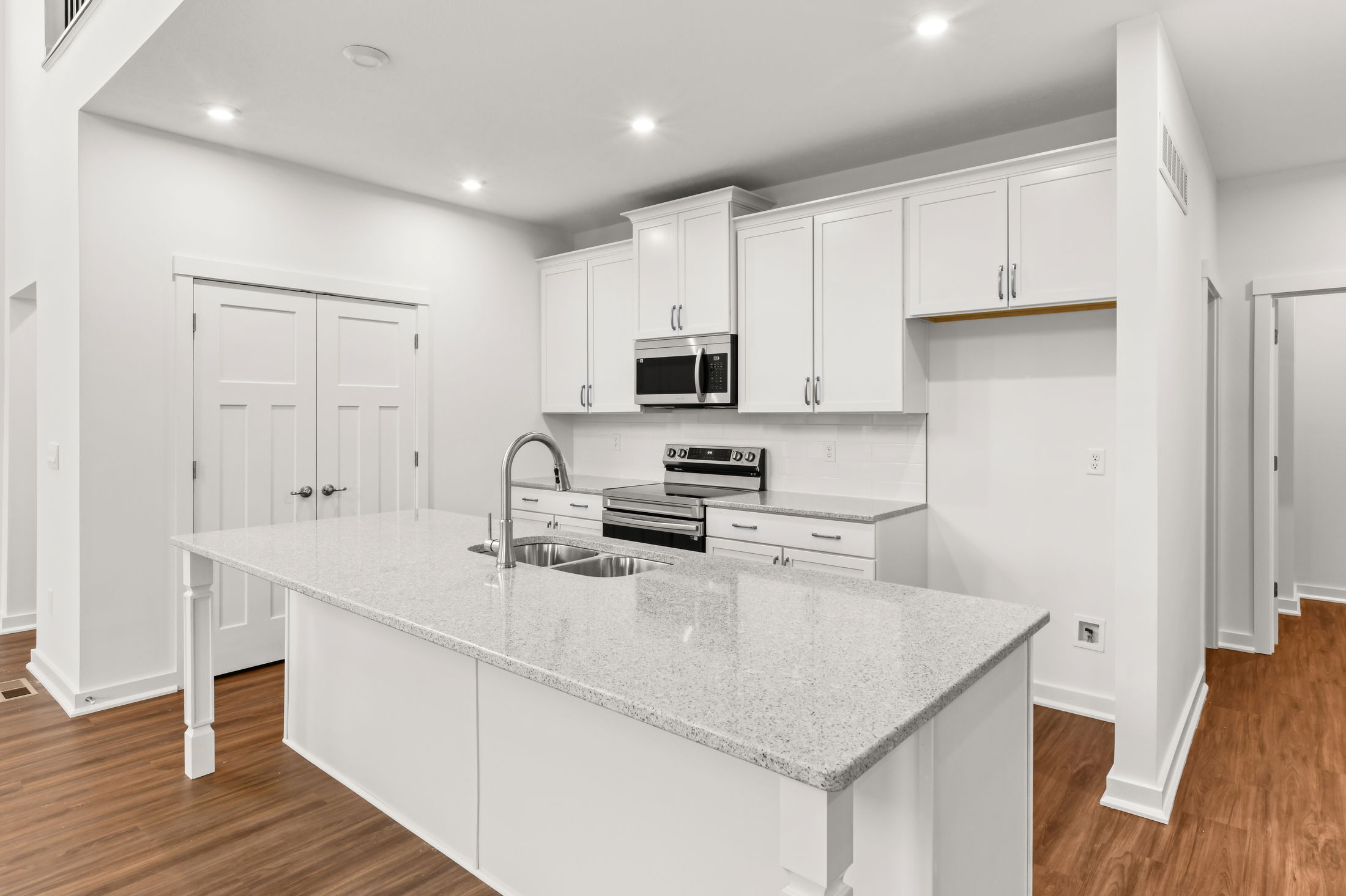 Modern white kitchen with granite countertops, stainless steel appliances, and hardwood flooring.