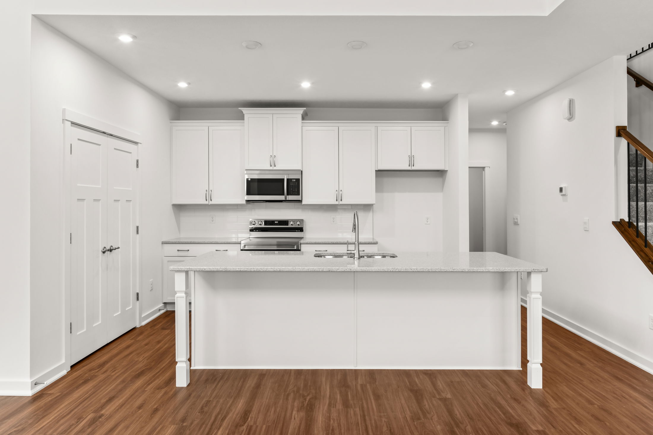 Sleek modern kitchen with white cabinets, stainless steel appliances, and a granite island countertop in a bright, spacious interior.