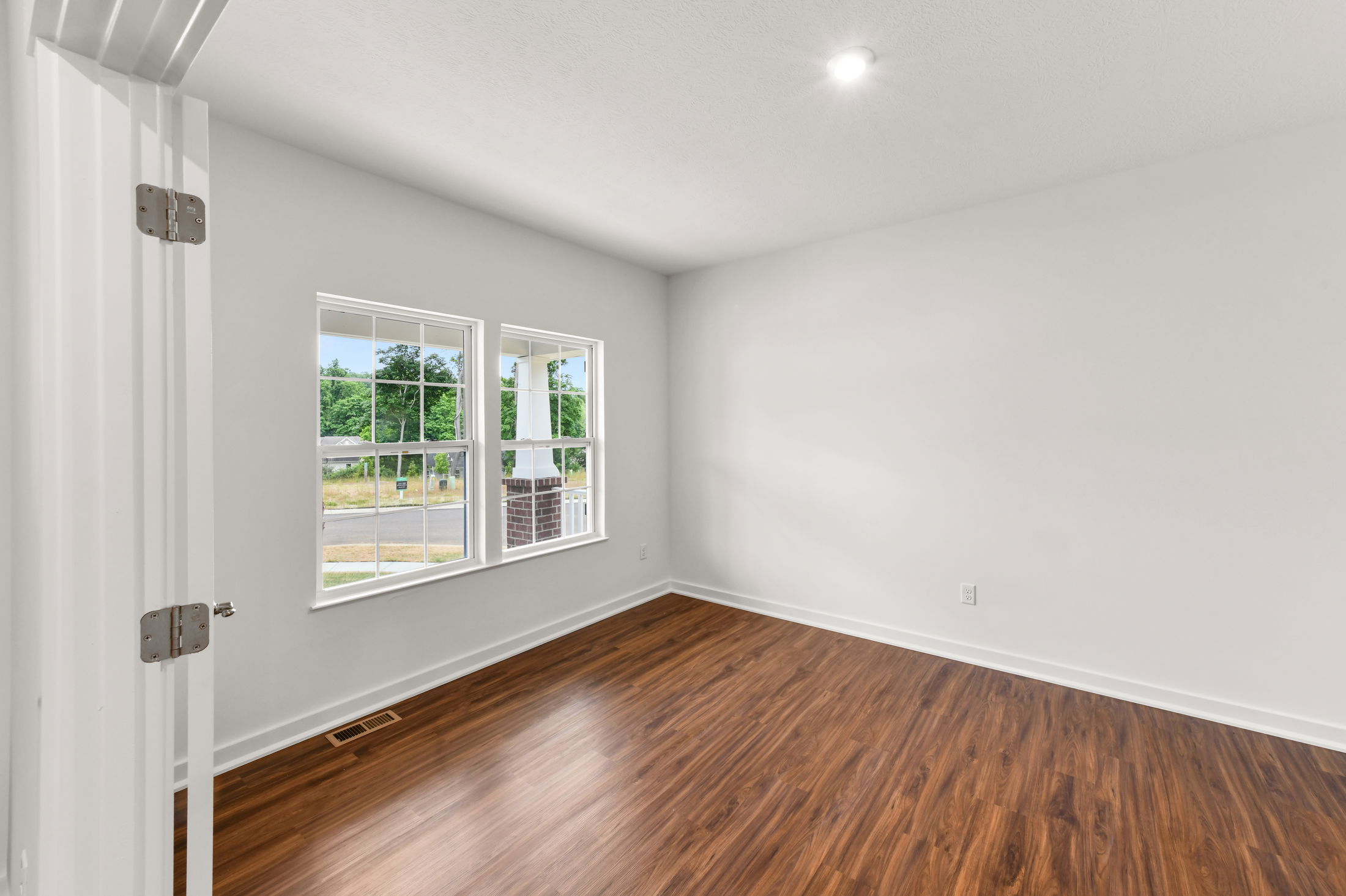 Empty white room with wooden floors, large windows, and natural light.