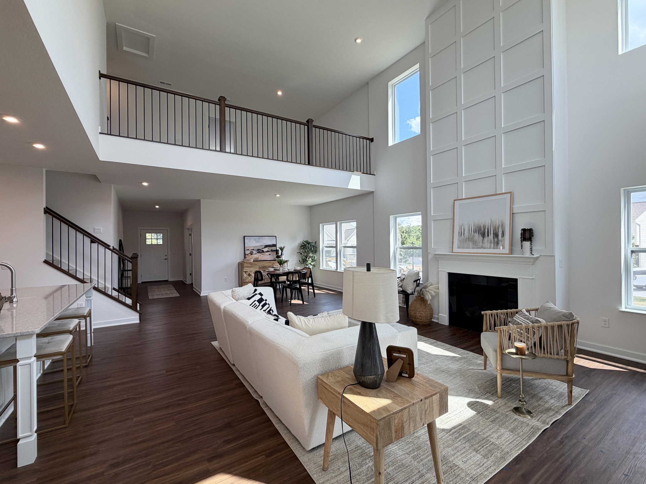 A modern living room featuring a two-story ceiling, large windows, a comfortable sofa, a coffee table, and a staircase.