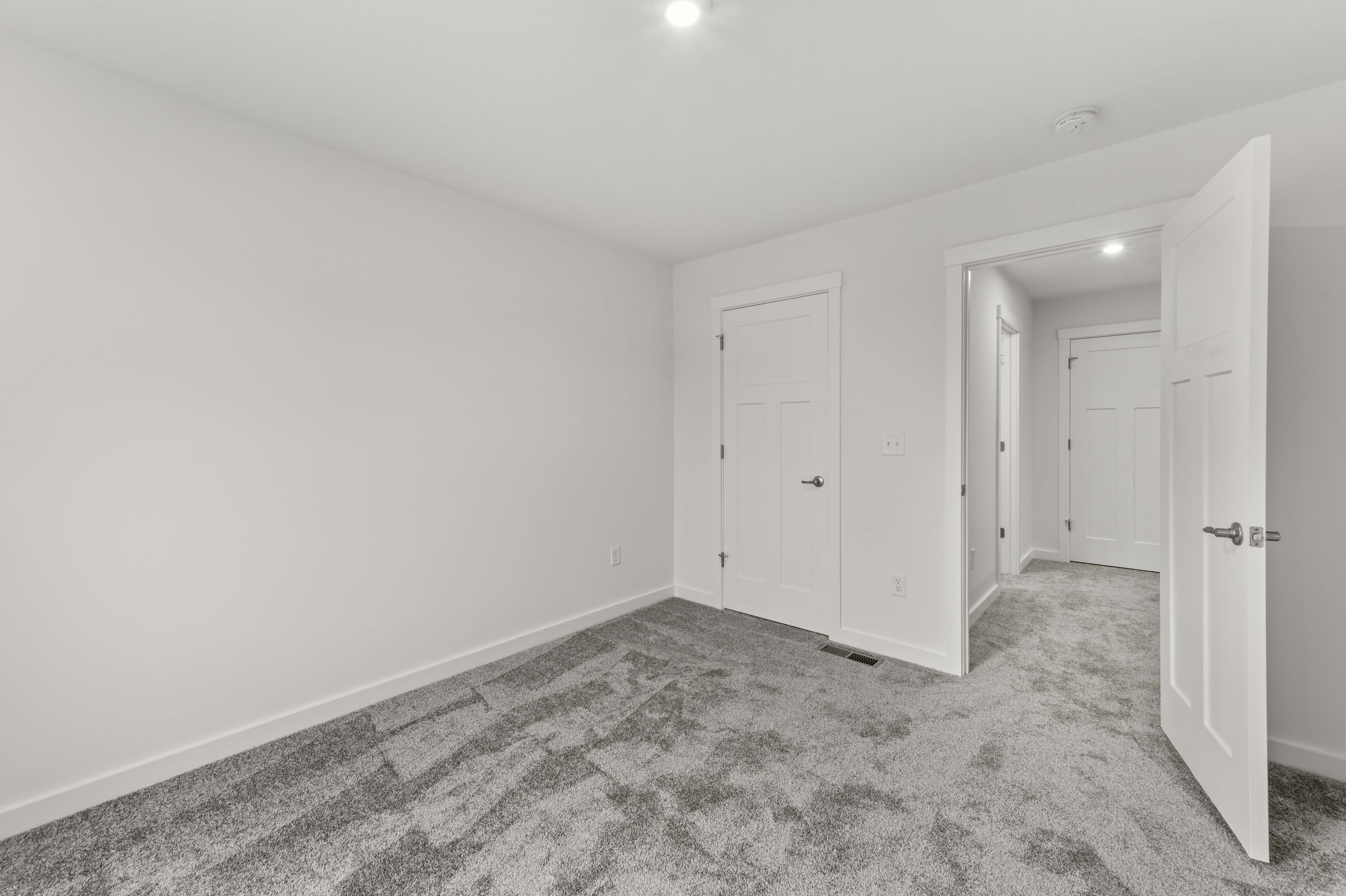 Minimalist empty room with gray carpet, white walls, and modern white doors, ideal for real estate and interior design concepts.