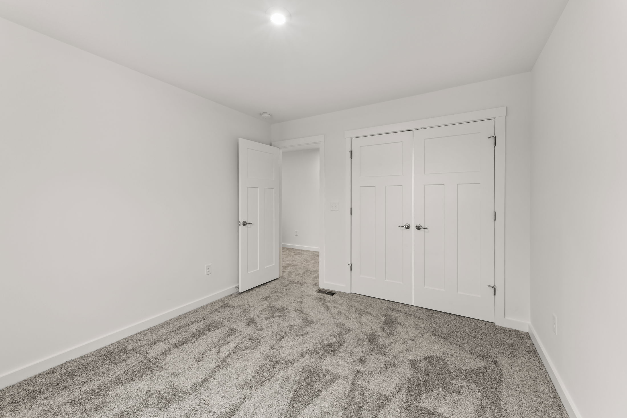 Empty bright bedroom with gray carpet, white walls, and a double-door closet.