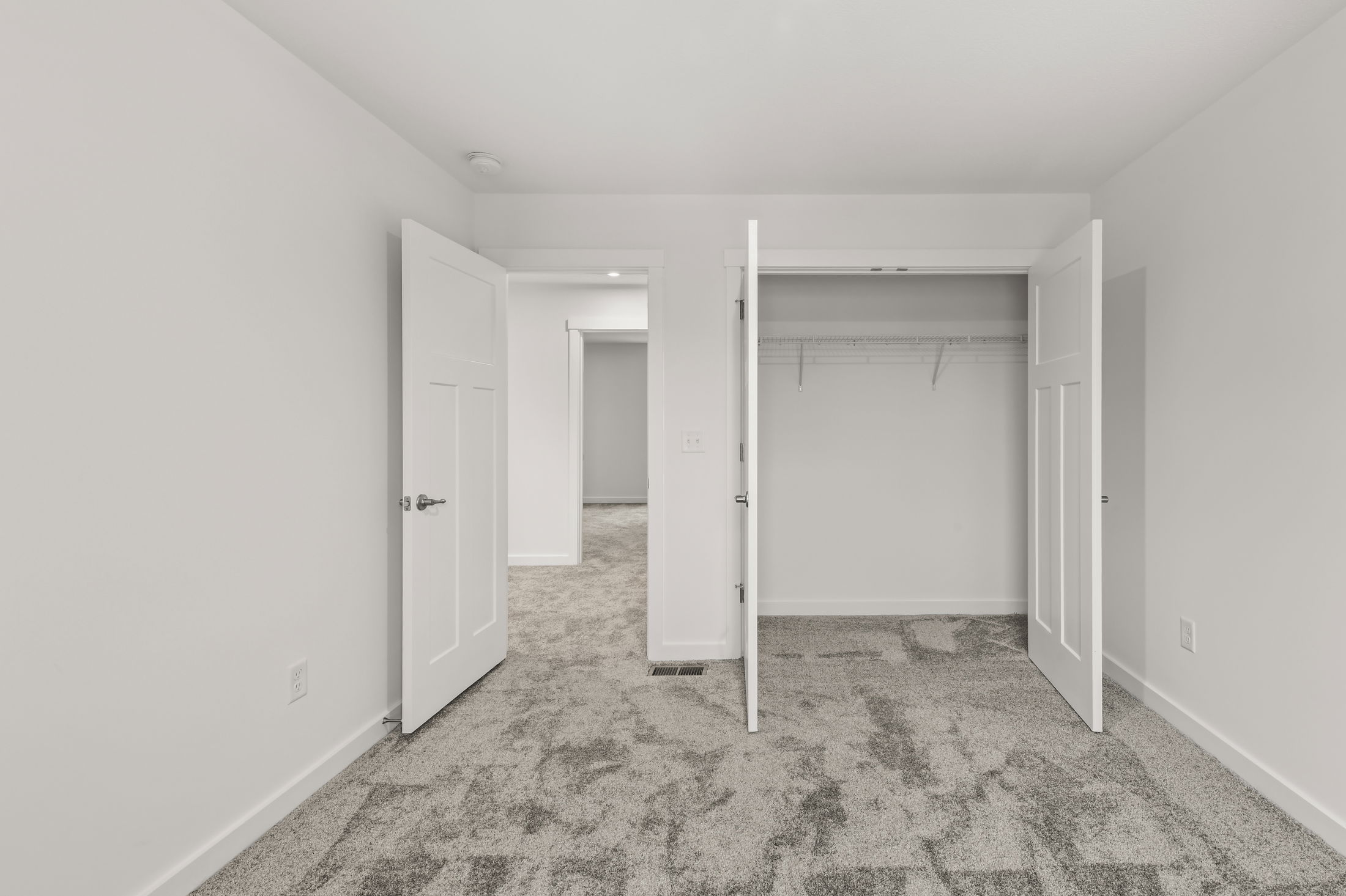Empty white bedroom with open closet and doors, showcasing plush gray carpet flooring.
