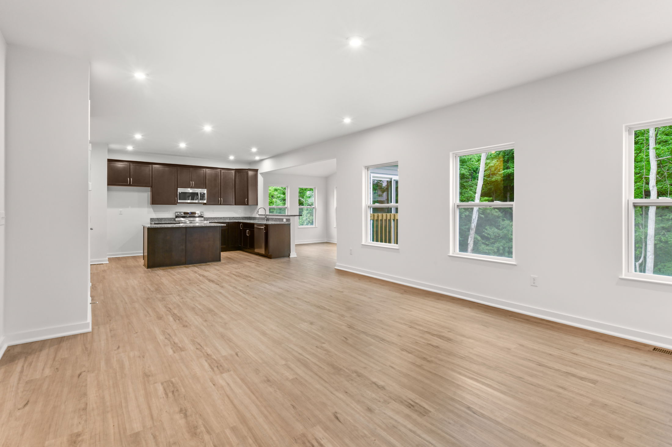 Spacious open-concept kitchen and living area with hardwood floors, modern cabinetry, and large windows overlooking greenery.