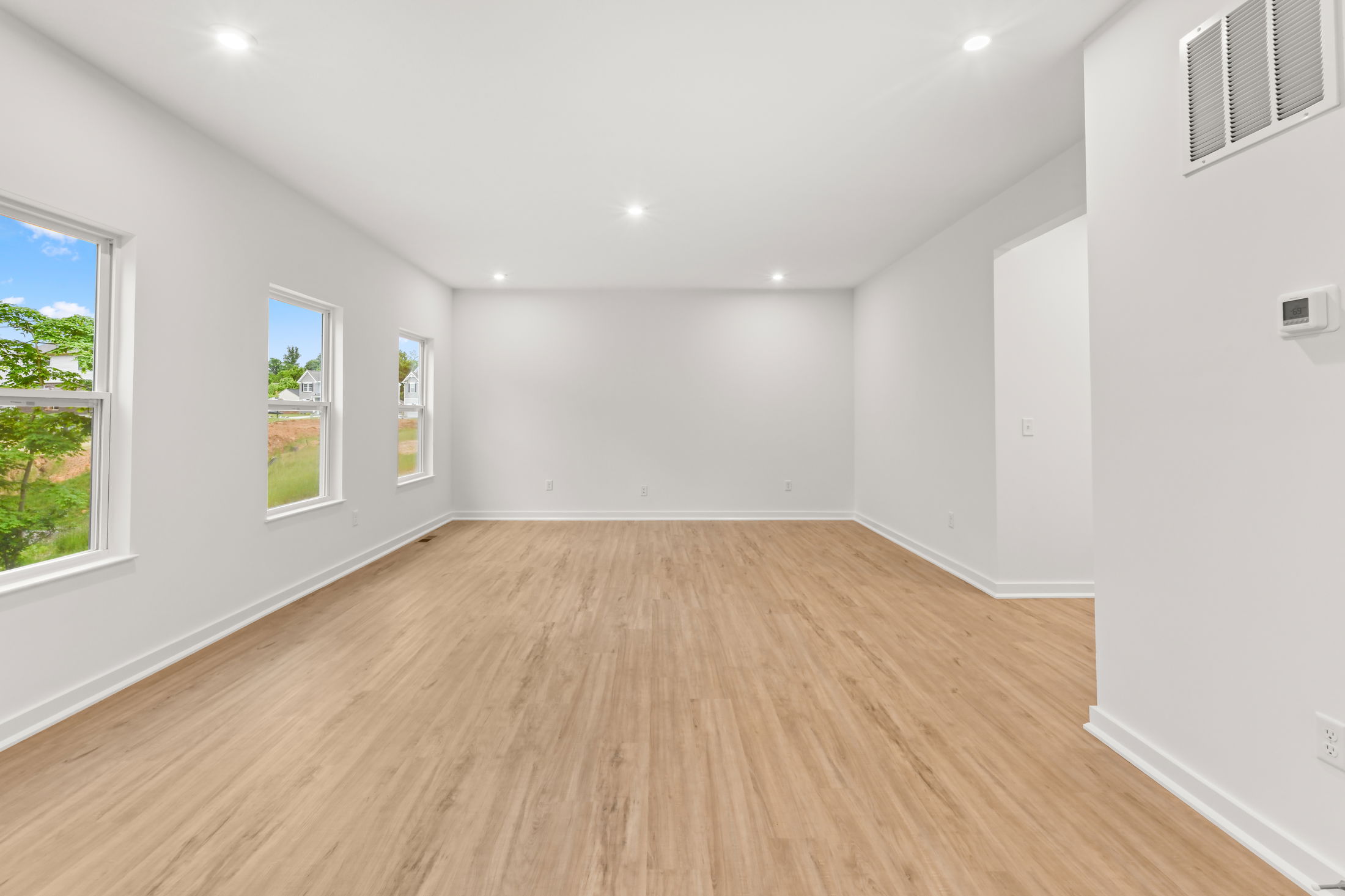 Bright, modern empty room with light wood flooring, white walls, and large windows providing natural light.