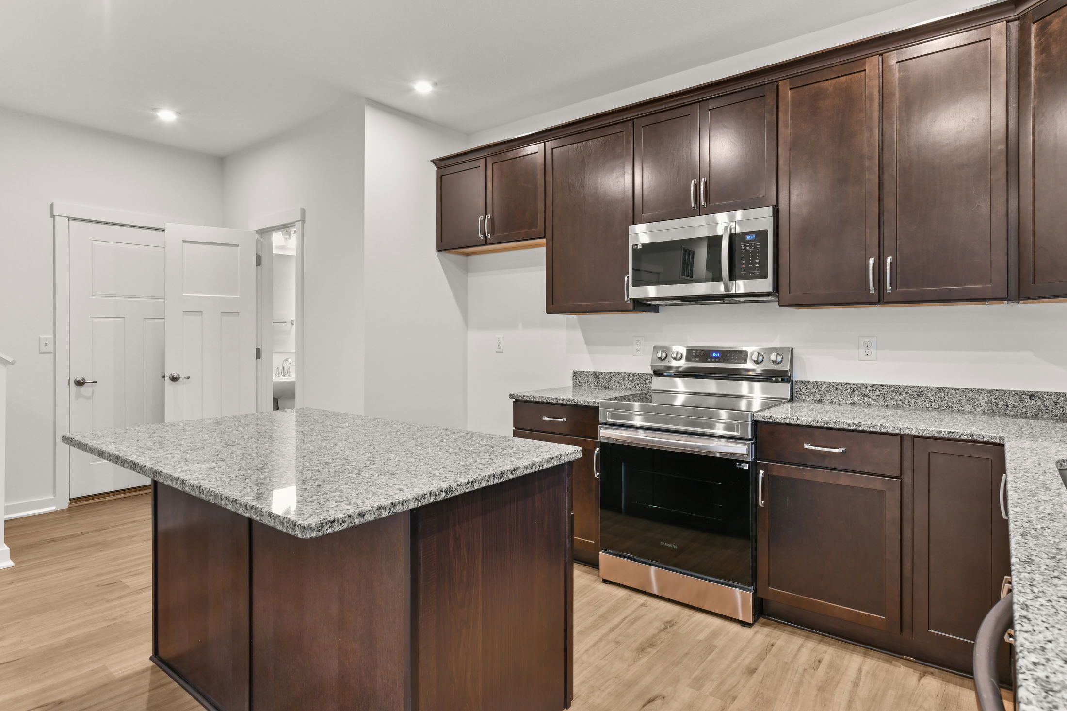 Modern kitchen with dark wood cabinets, stainless steel appliances, and a granite countertop island.