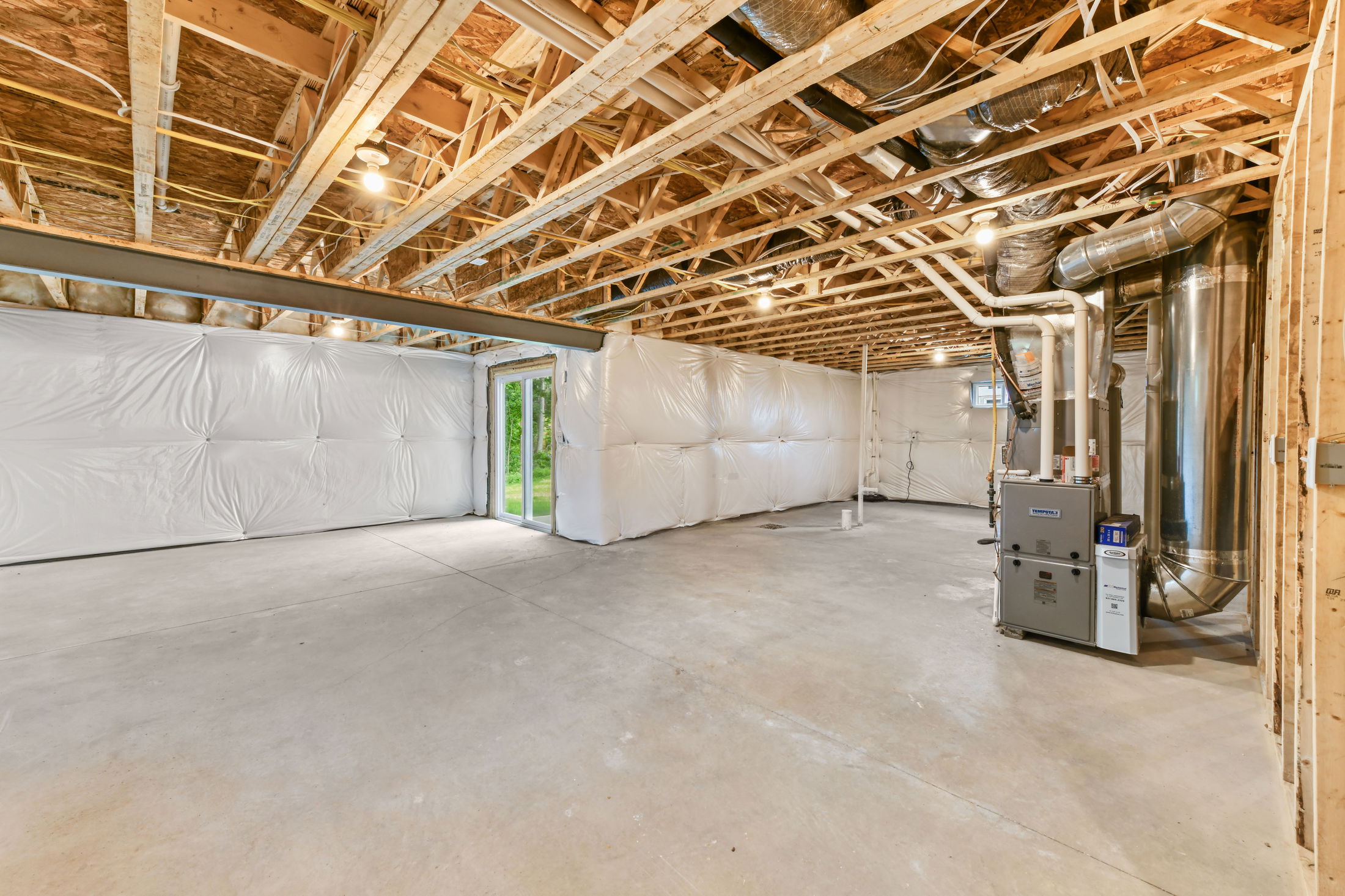 Unfinished basement with exposed beams, ductwork, and concrete flooring, featuring a sliding glass door and HVAC system.
