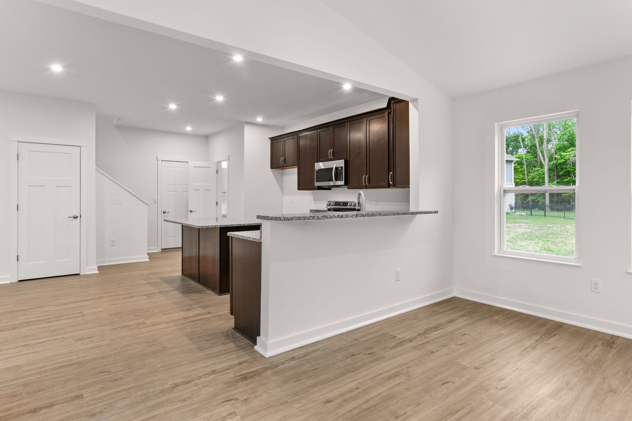 Modern open-concept kitchen with dark wood cabinets, granite countertops, and hardwood flooring in a bright, spacious interior.
