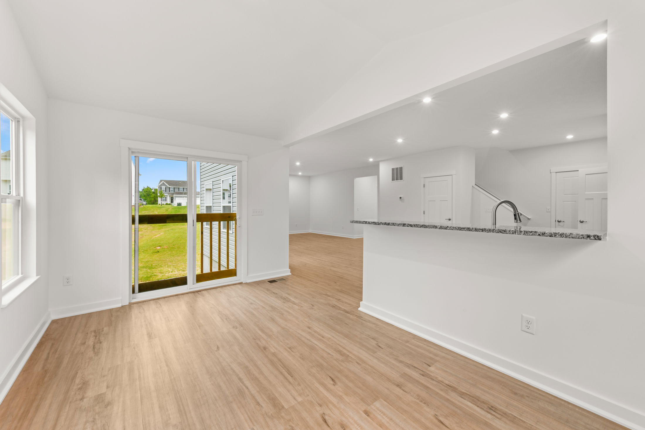 Bright, modern open-concept living room and kitchen with hardwood floors and sliding glass doors leading to a grassy backyard.