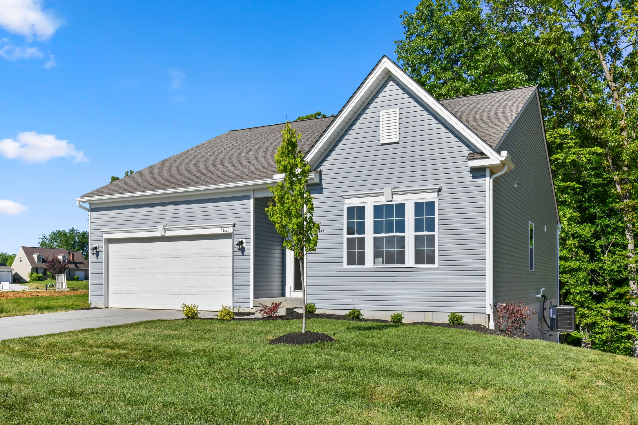 Modern gray single-story house with a two-car garage, front lawn, and clear blue sky.