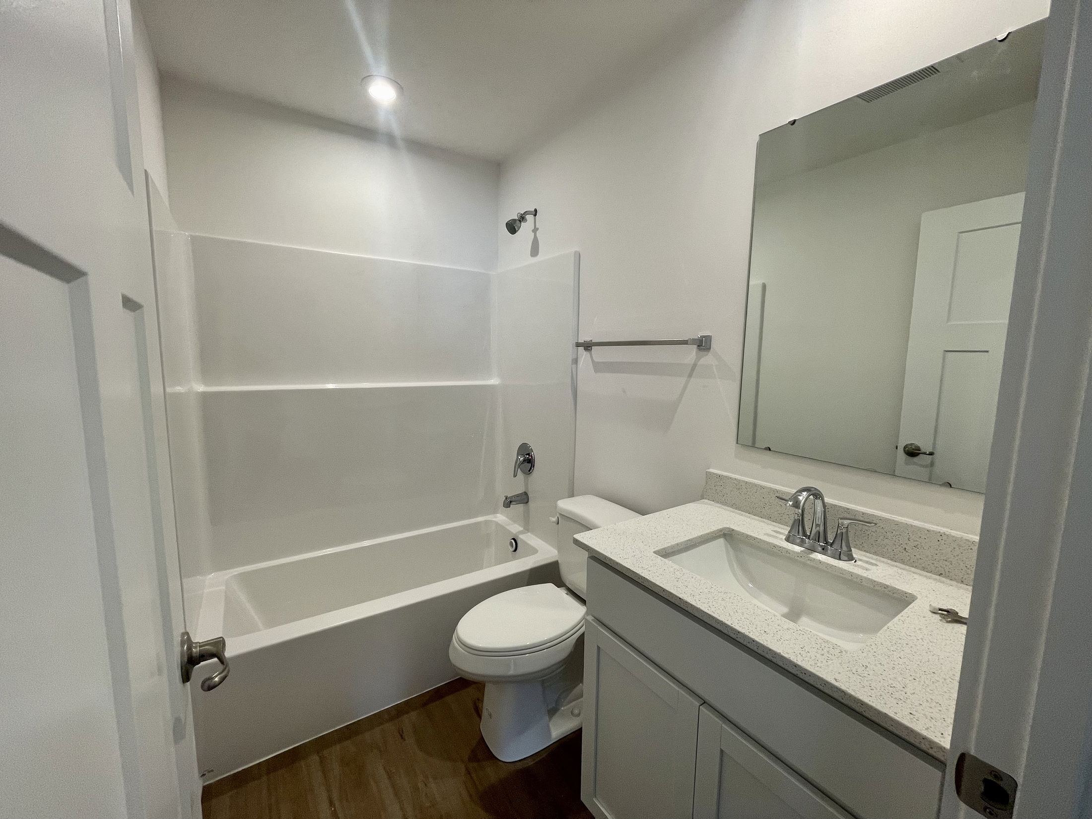 Modern bathroom with a white bathtub, sink, and toilet, featuring wooden flooring and recessed lighting.