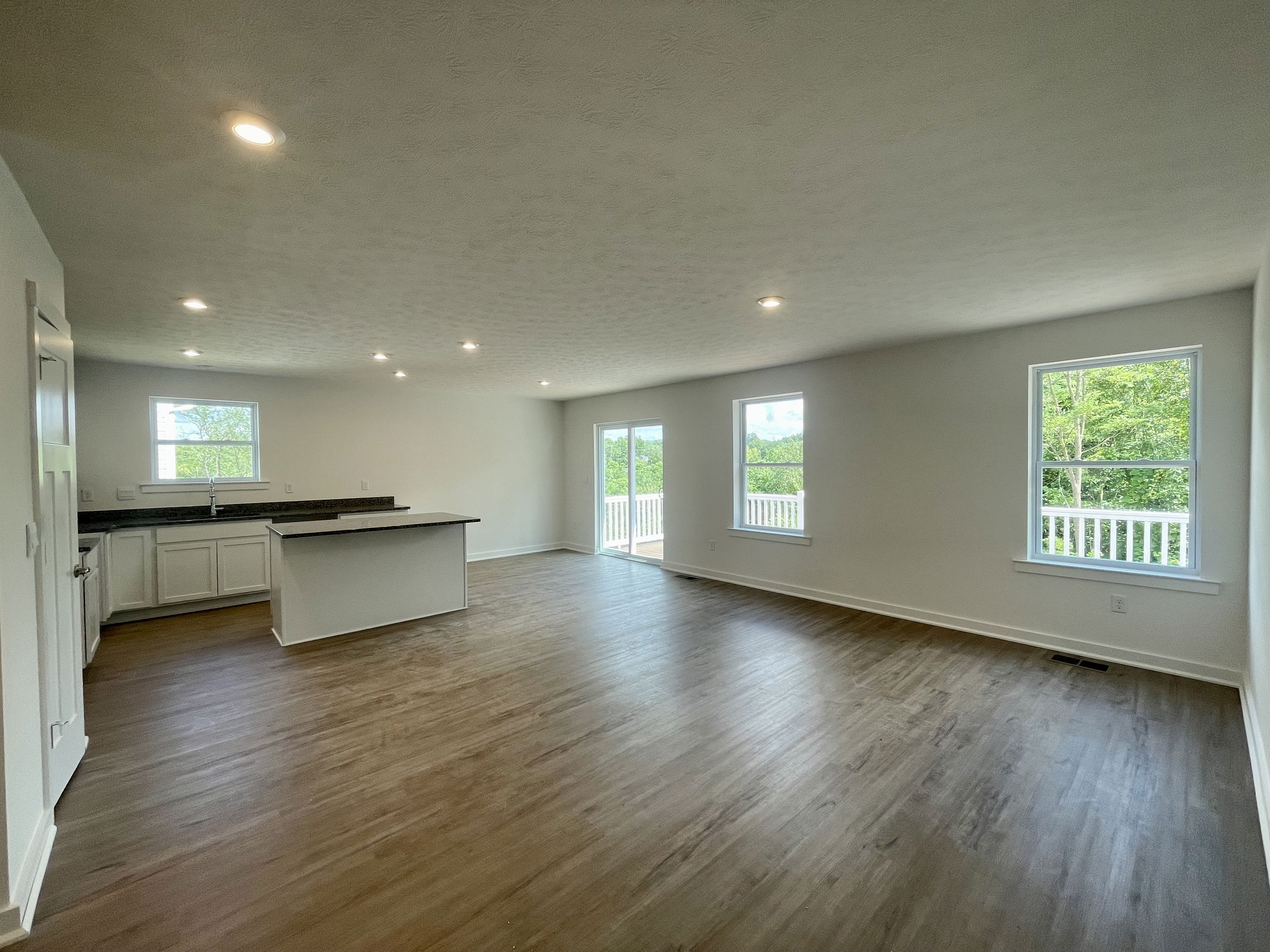 Spacious open-concept living area with hardwood flooring, modern kitchen island, and large windows in a bright, newly renovated home.
