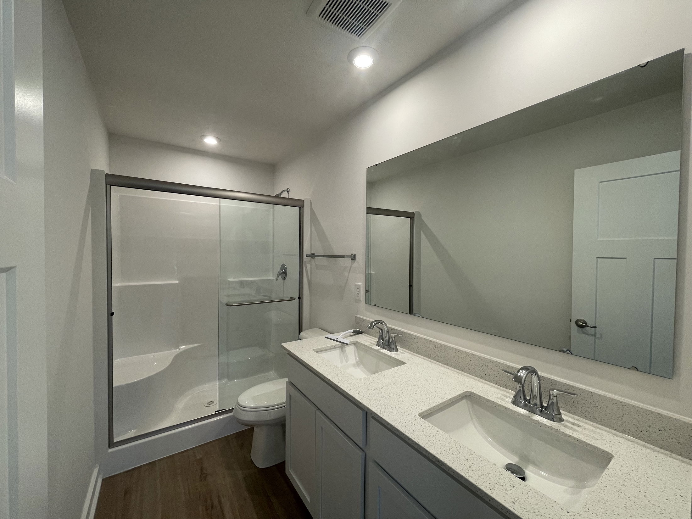 Modern bathroom with double sinks, large mirror, and glass-enclosed shower.