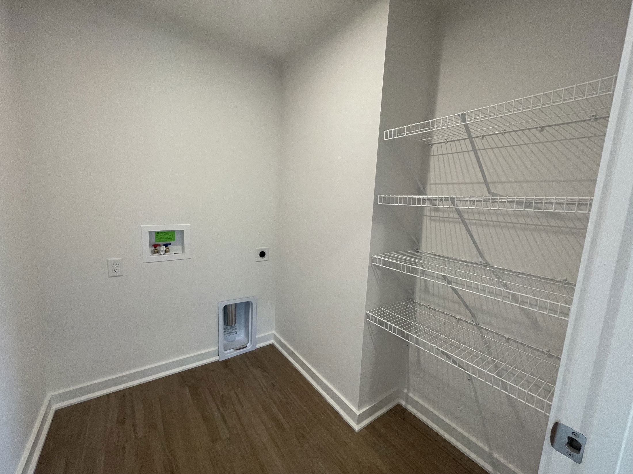Laundry room with white walls featuring an installation area for washer and dryer, alongside empty white wire storage shelves.
