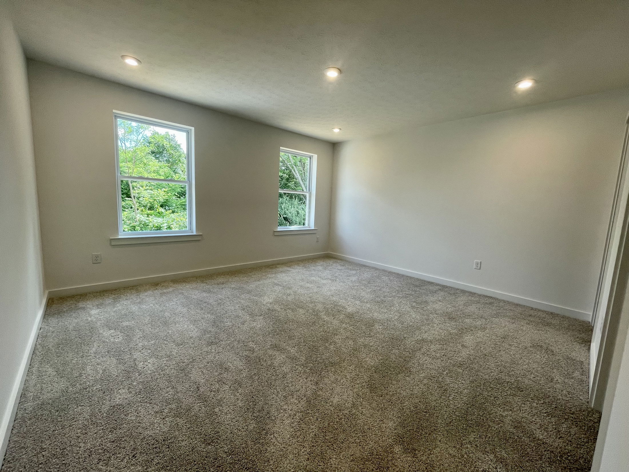 Spacious empty room with carpet flooring, white walls, large windows, and recessed lighting.