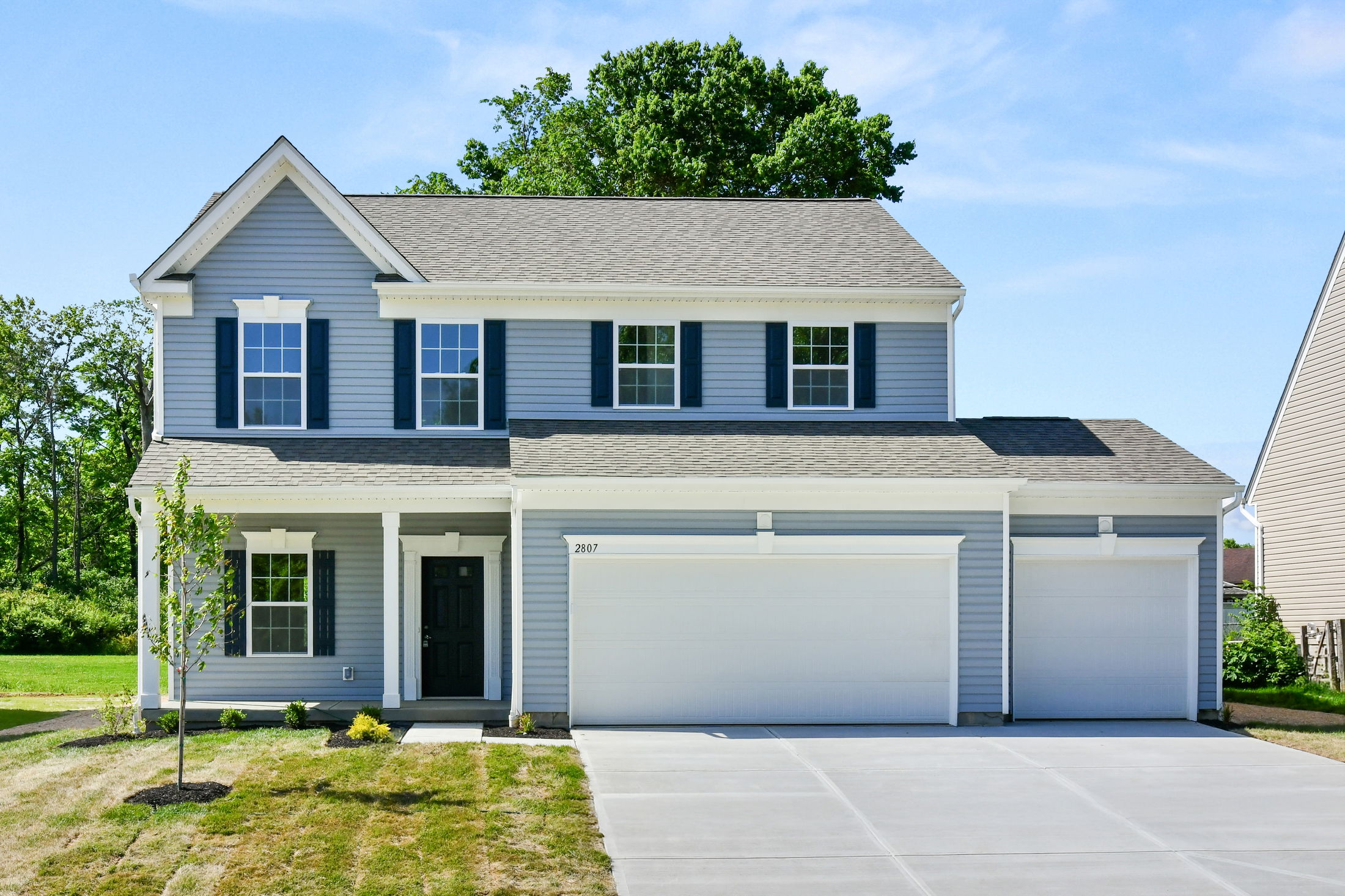 Modern two-story gray suburban house with three-car garage and lush green lawn on a sunny day.
