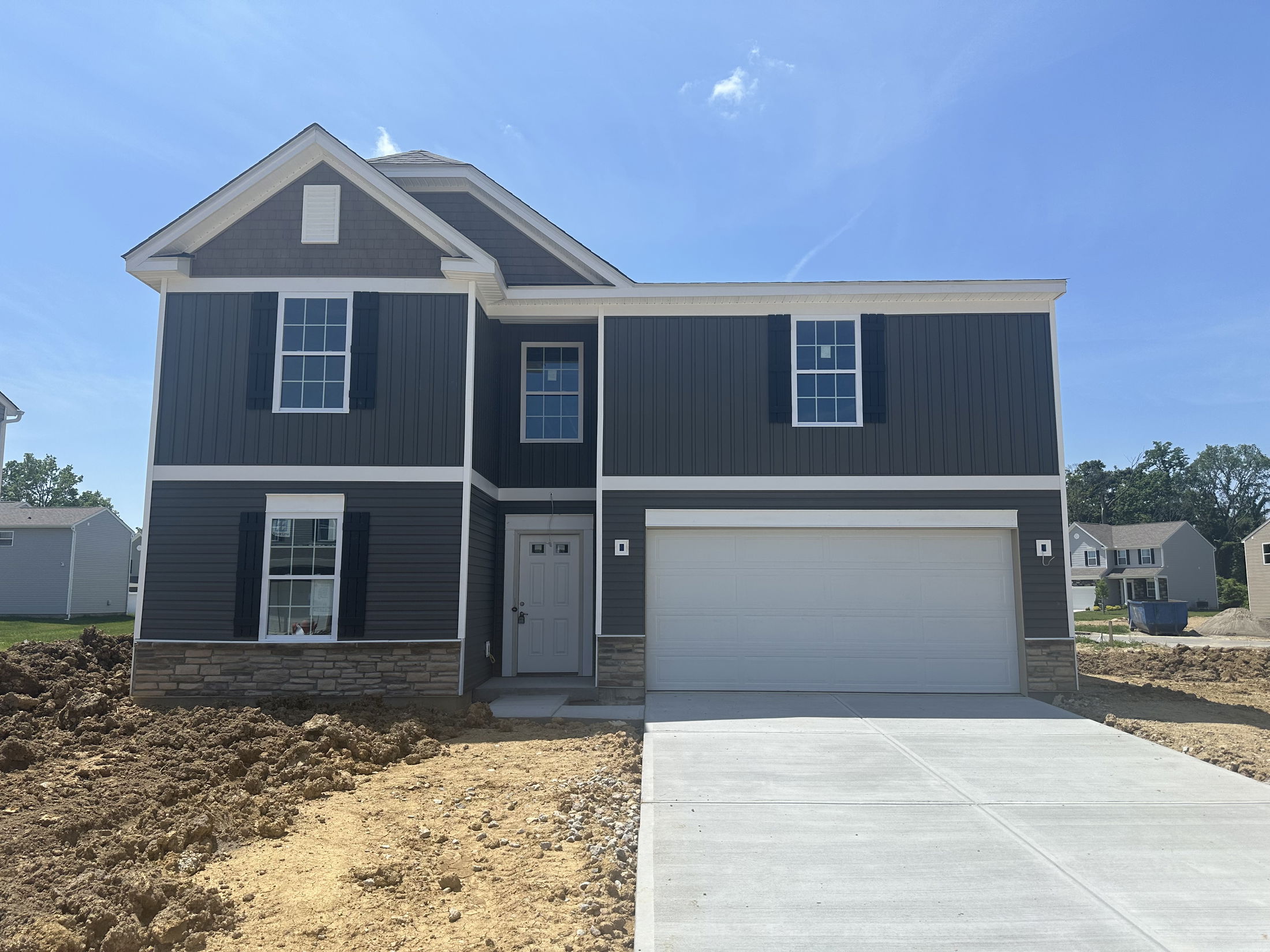 Newly constructed two-story home with dark siding, stone accents, and a double garage on a sunny day.