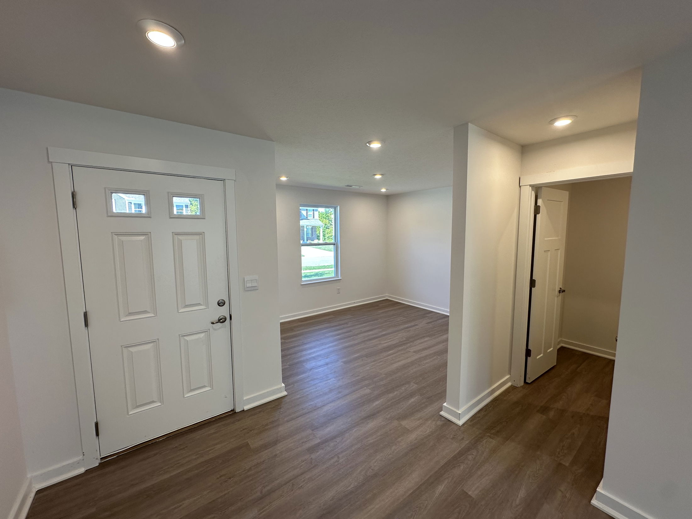 Modern entryway with white walls, wood flooring, and recessed lighting in a bright, open space.