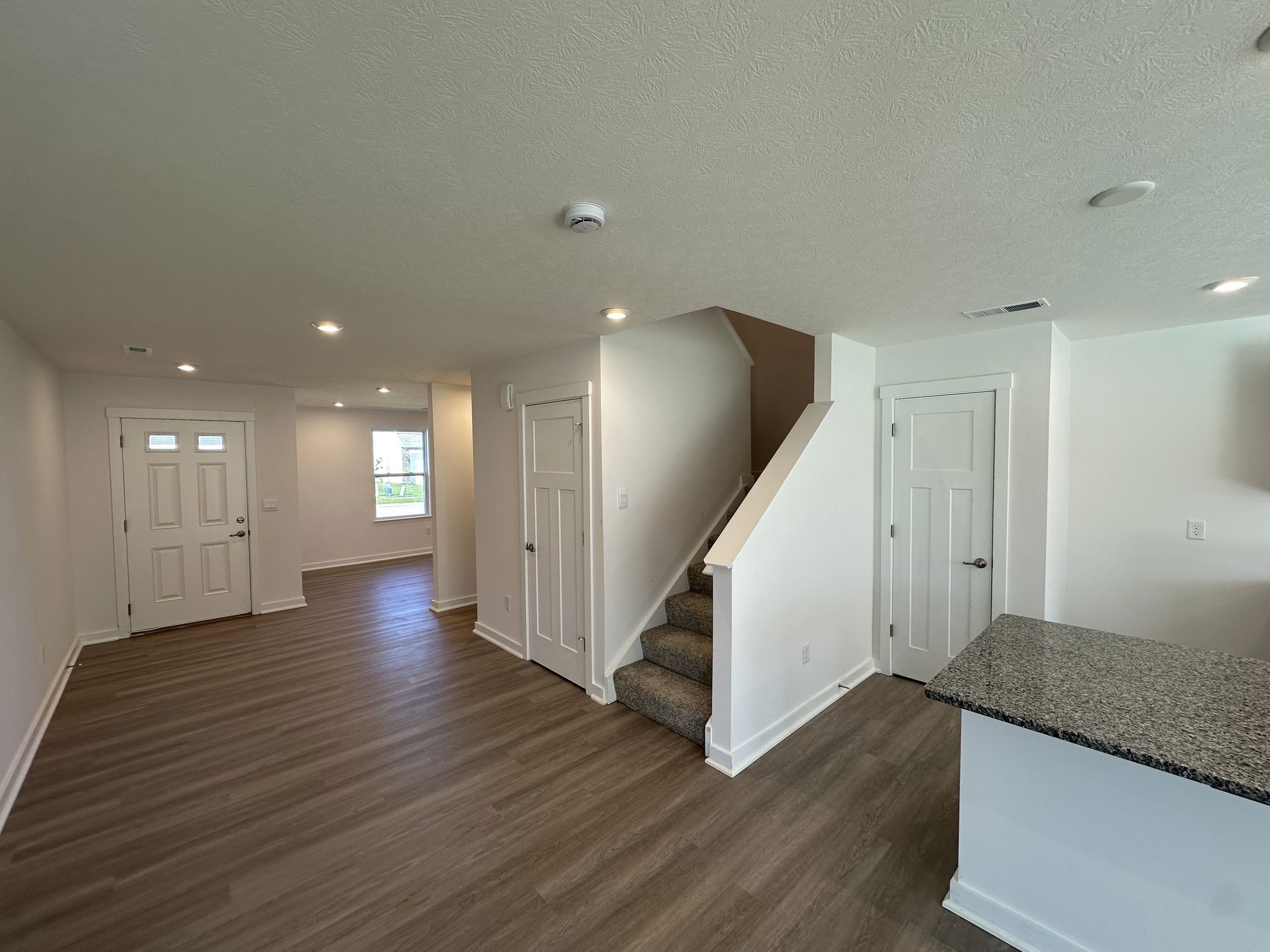 Spacious modern entryway and living area with wood flooring, white walls, and carpeted stairs leading to the upper level.