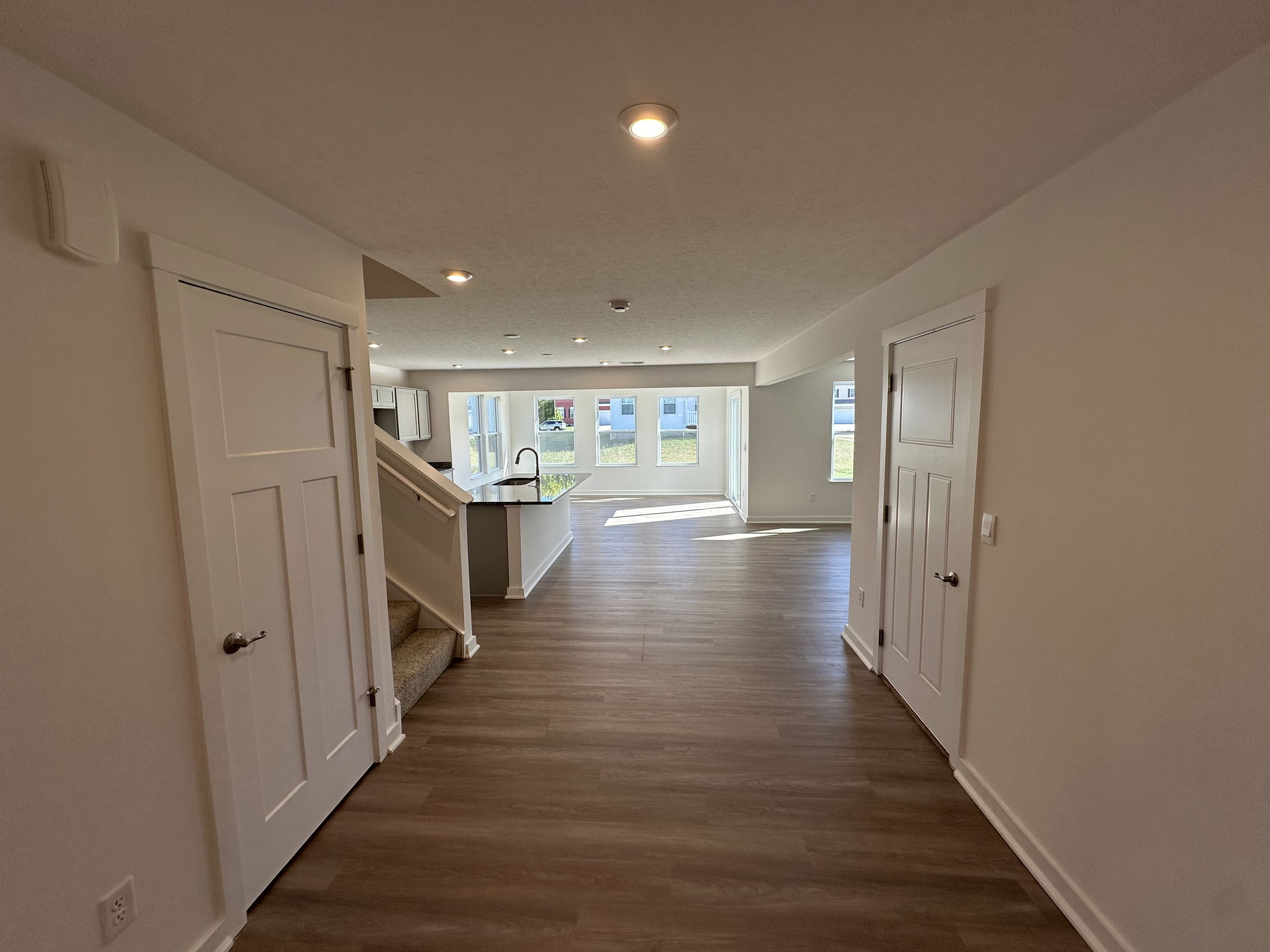 Modern open-concept living area with hardwood floors, staircase, and bright kitchen space.