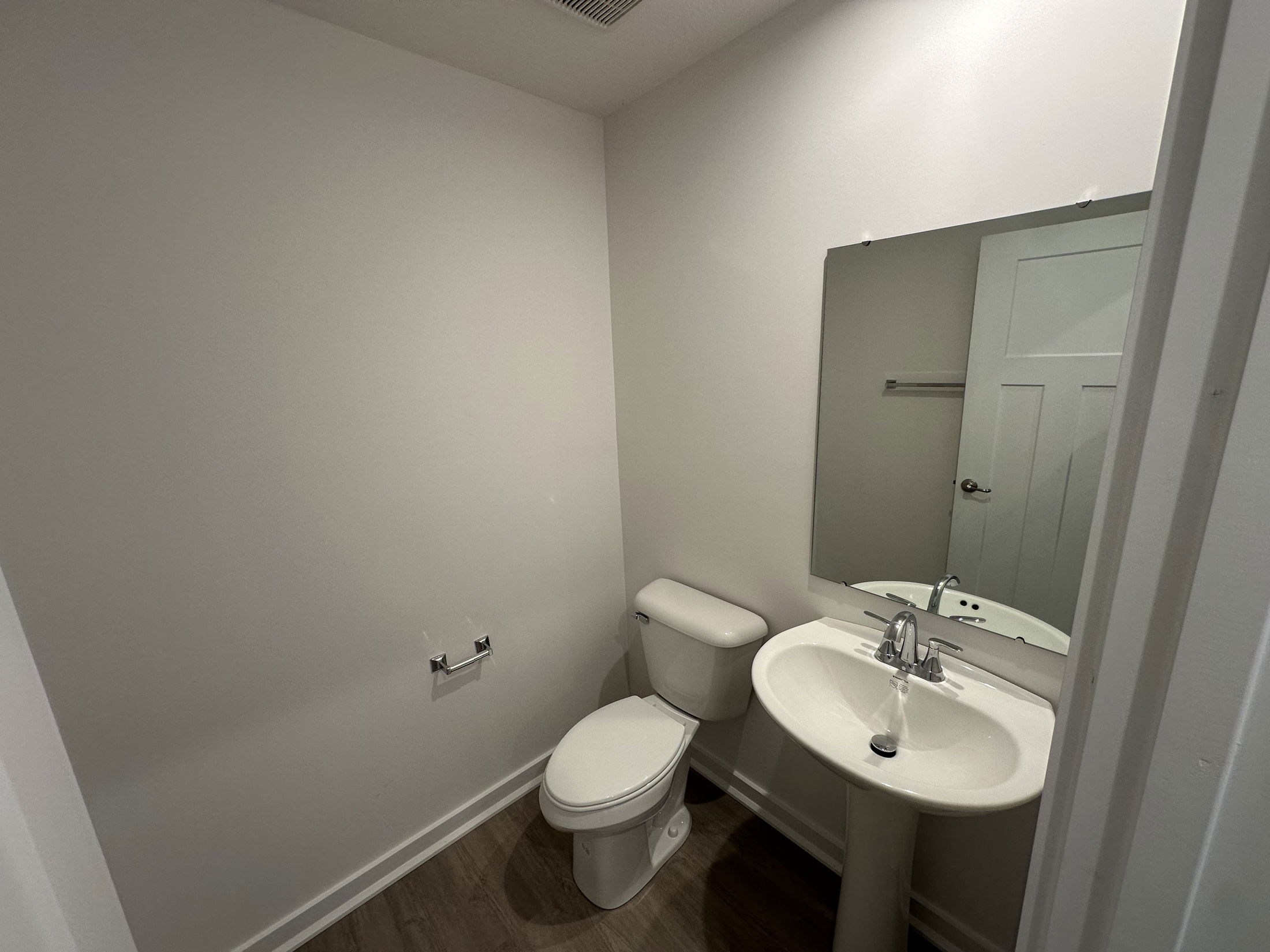 Small modern bathroom interior with white toilet, pedestal sink, and large mirror.